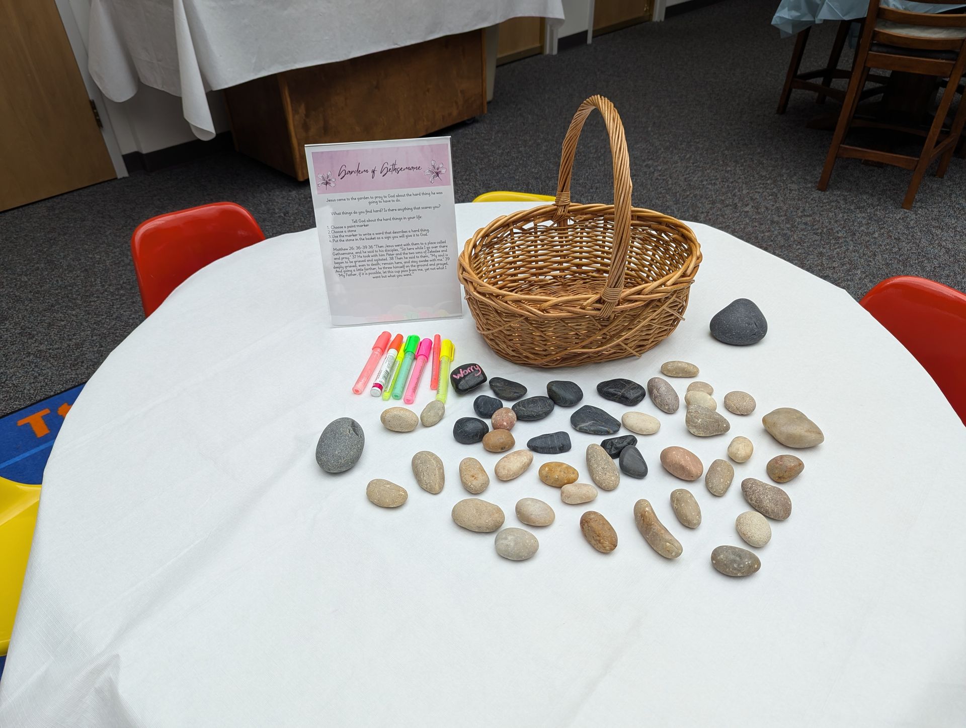 Display of painted stones, markers, and a wicker basket on a white table at a craft fair