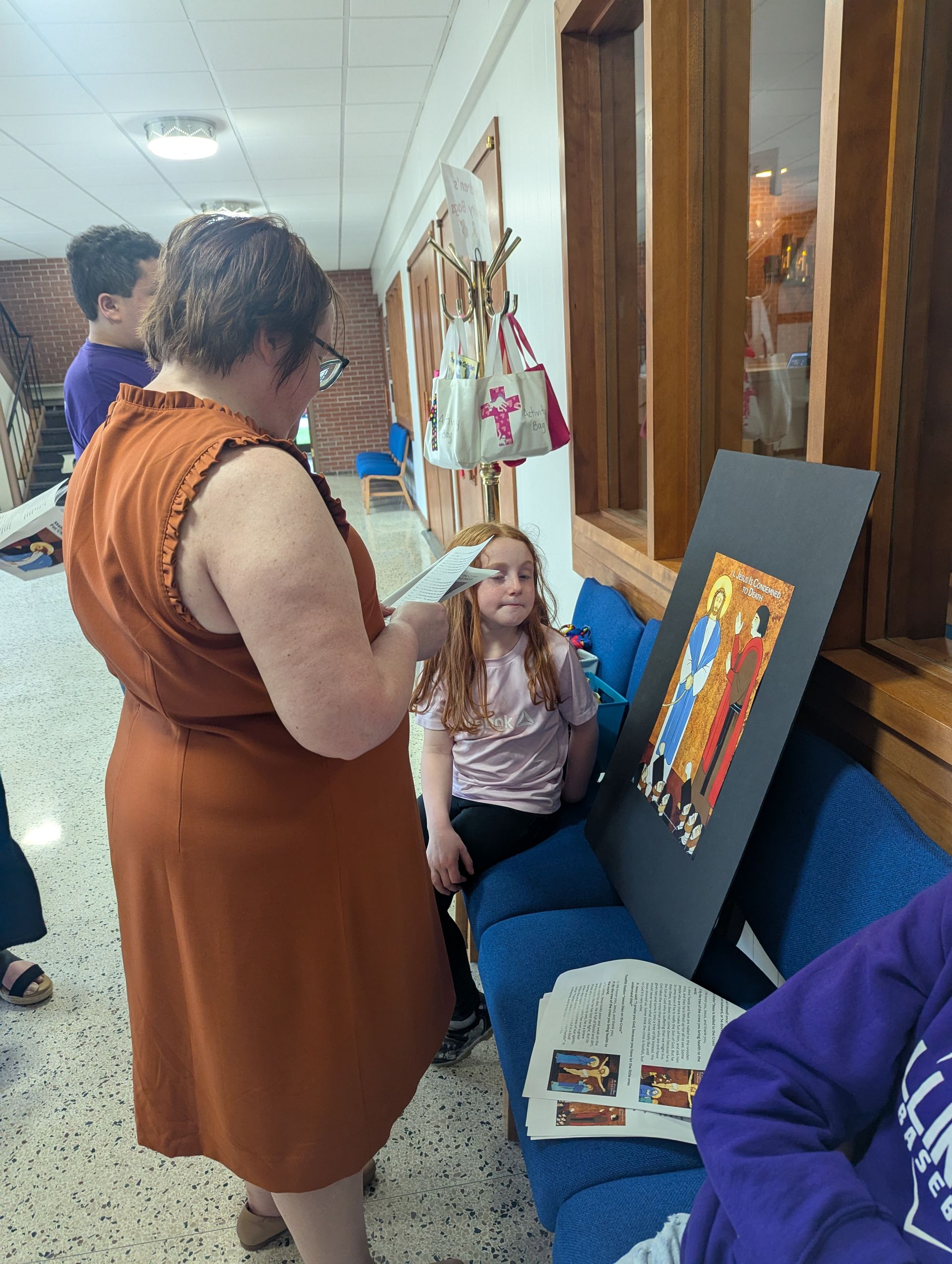 People gathered in a hallway viewing colorful artwork displayed on a chair and leaning against the wall.