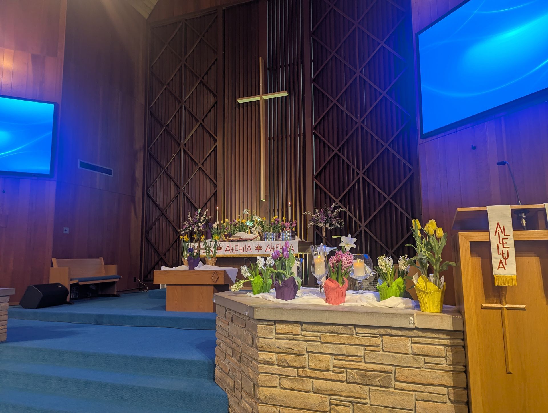 Church altar with flowers and candles, blue-lit sanctuary, and a wooden lectern on the right.