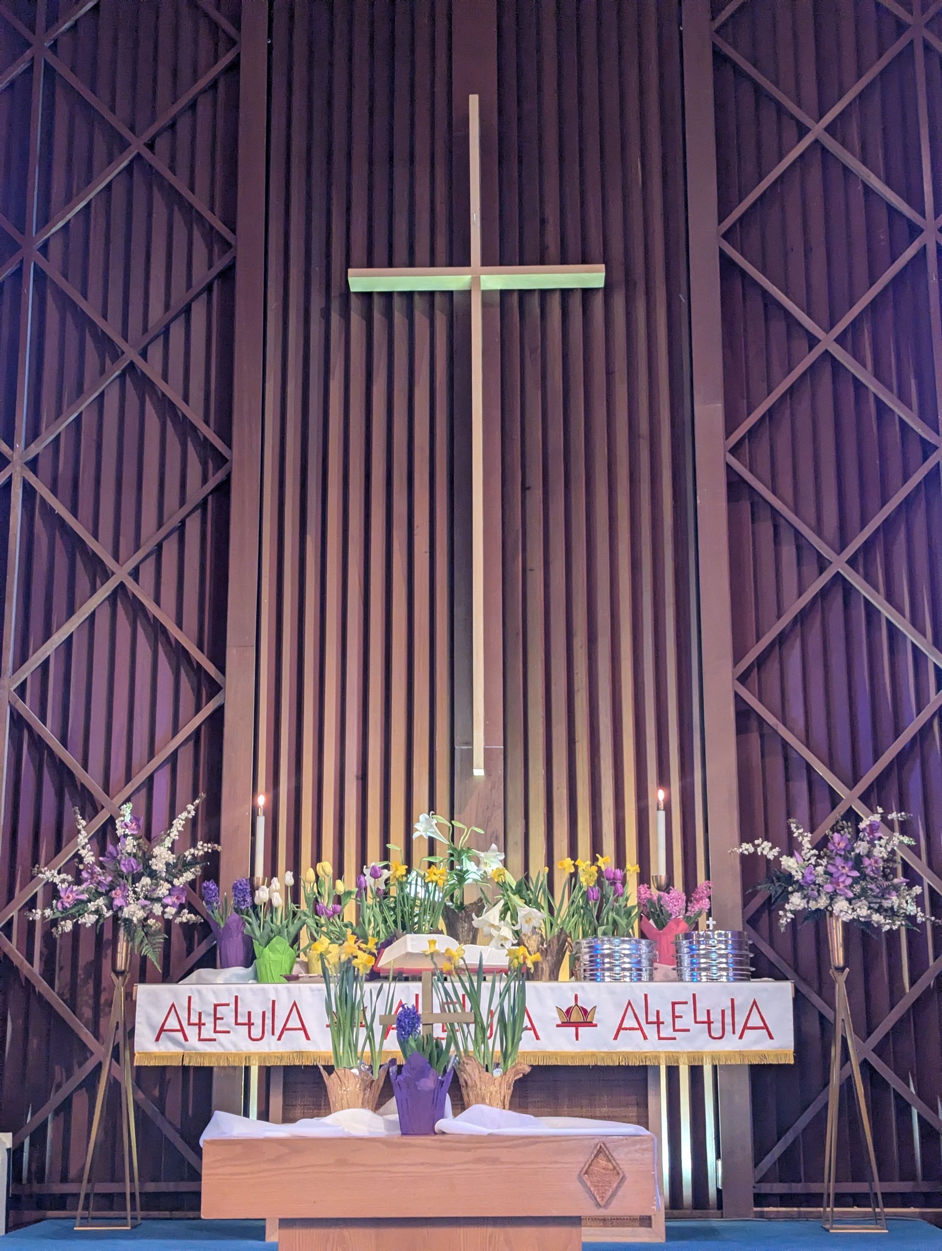 Church altar with a large cross, flowers, candles, and purple drapes in the background.