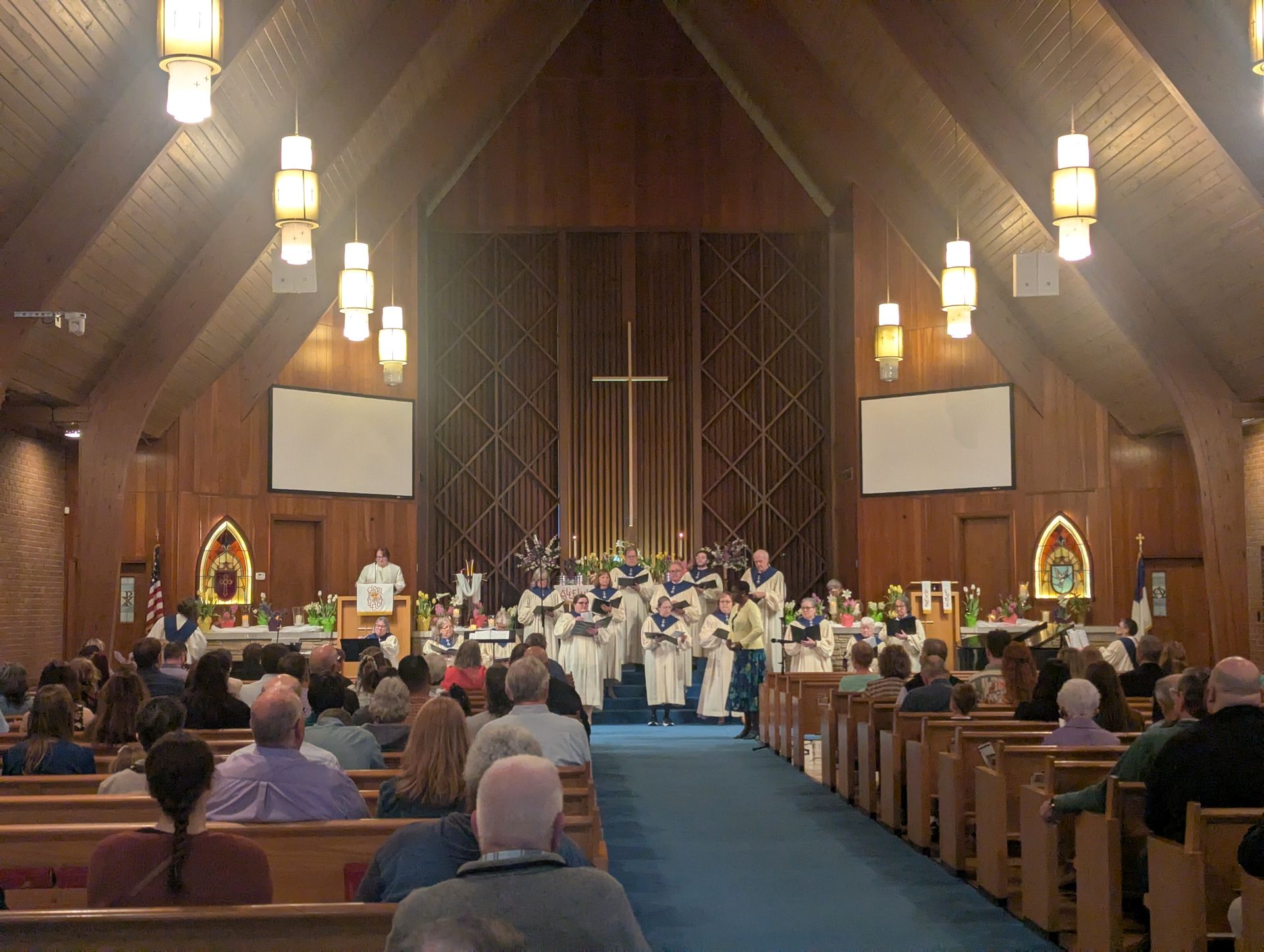 Choir performing in a church sanctuary with pews full of seated attendees under hanging lights.