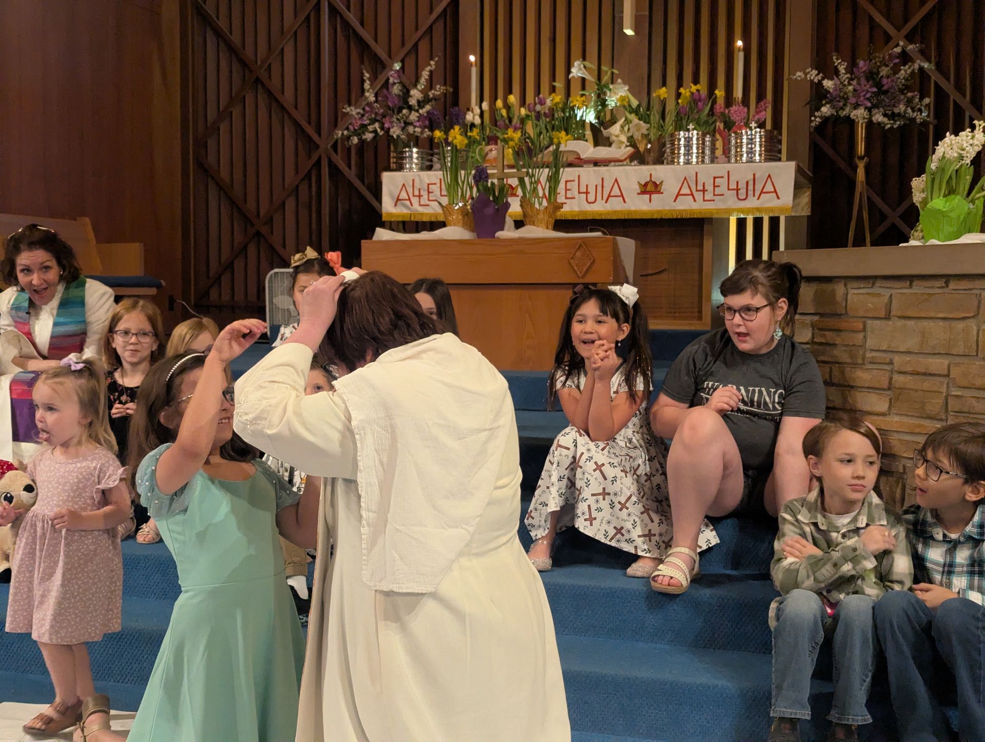 Children and adults dance and clap in front of an altar in a church hall