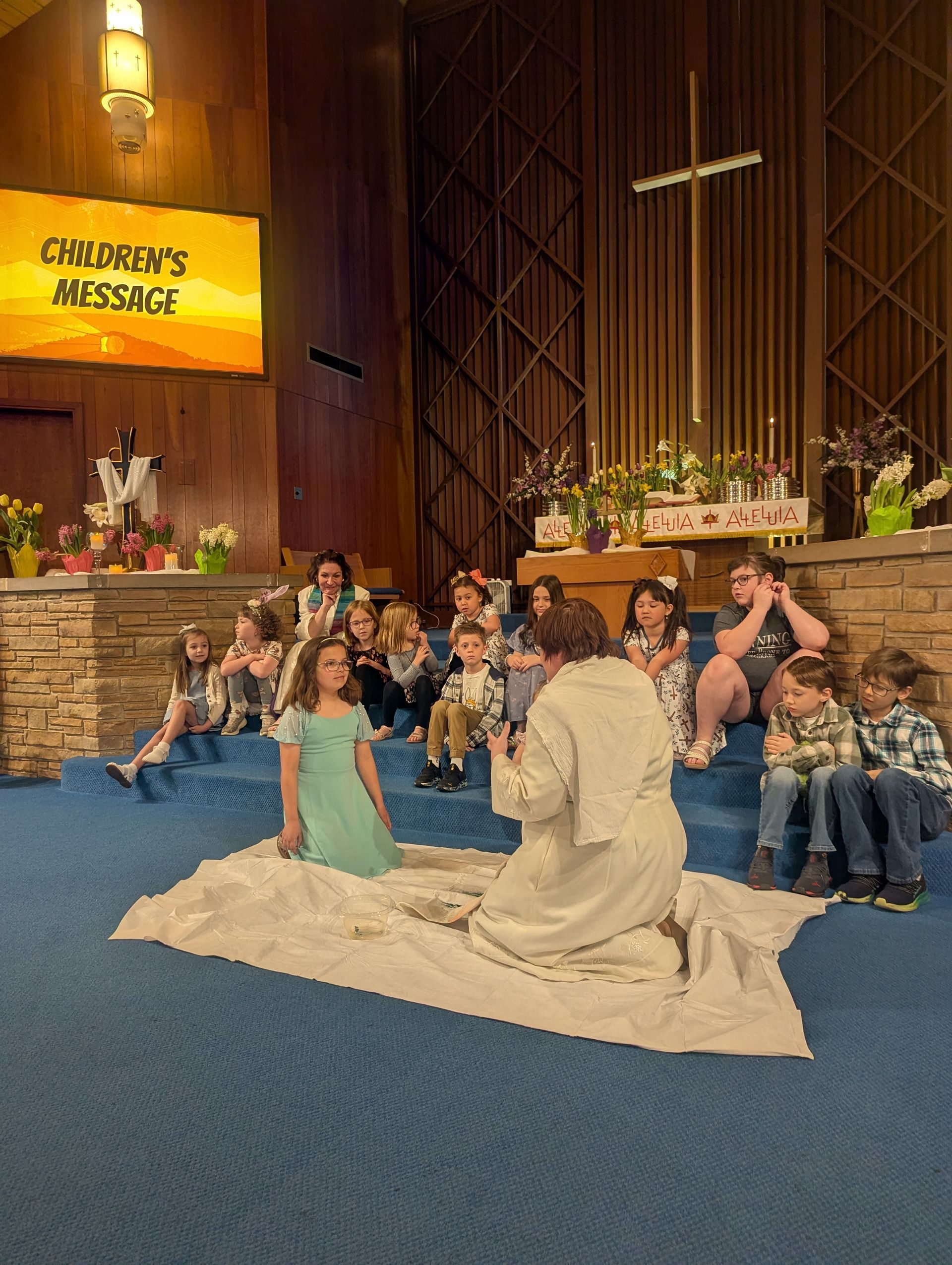 Children’s Message gathering in a church sanctuary, with children seated around a person in a cream outfit.