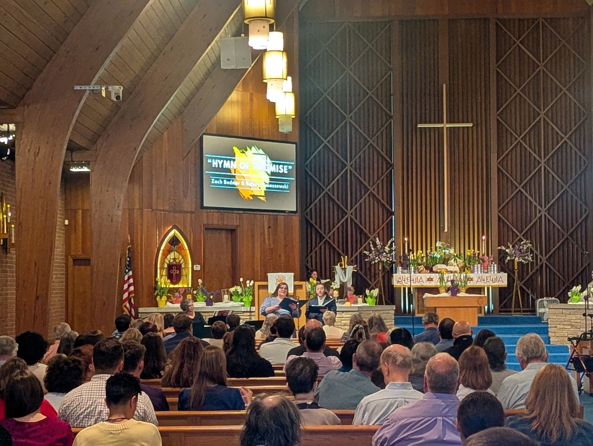 Church service in a wood-paneled sanctuary with congregation seated and a choir near the altar