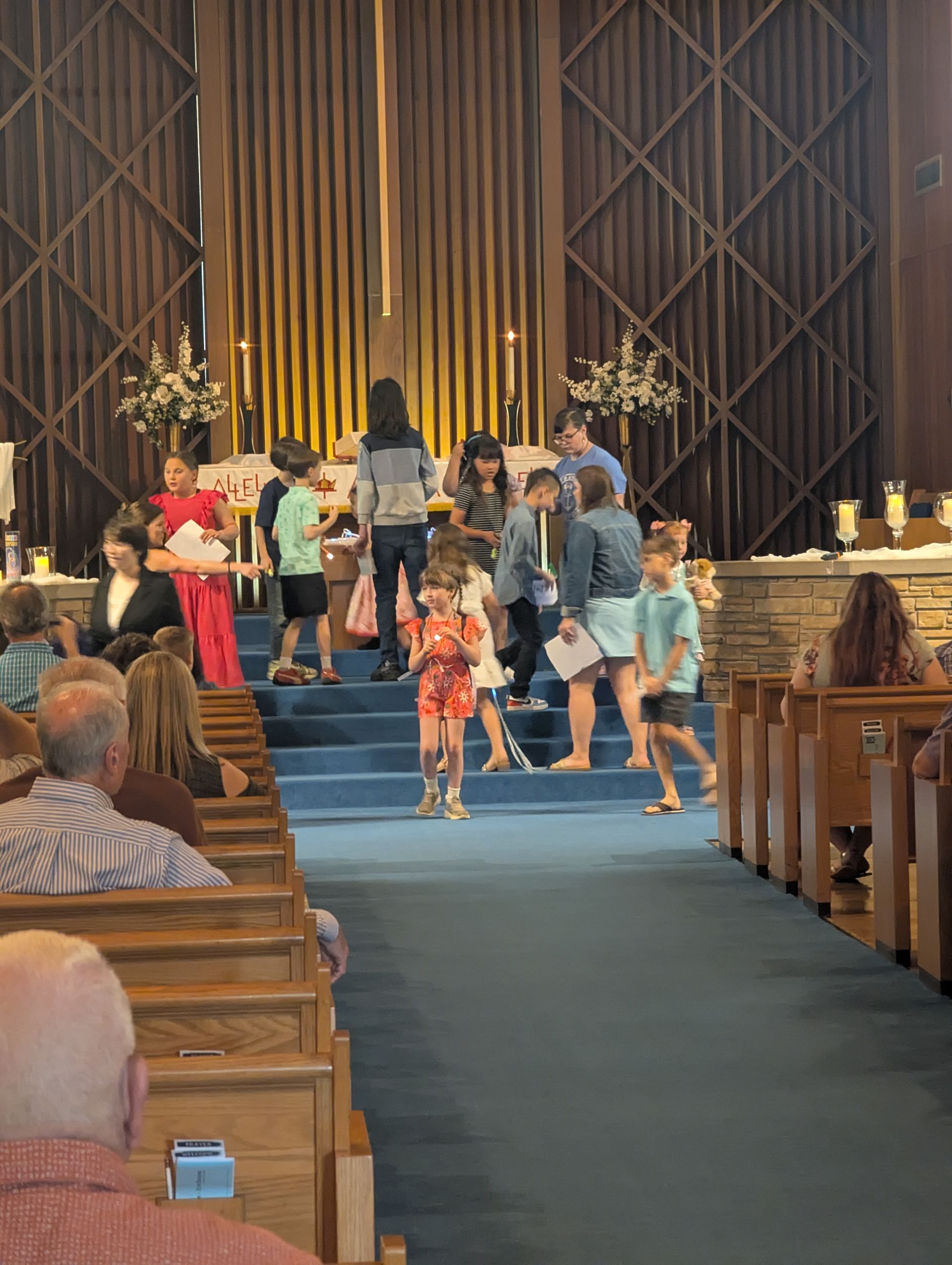 People walking up the blue-carpeted aisle in a church toward the altar with candles and flowers.