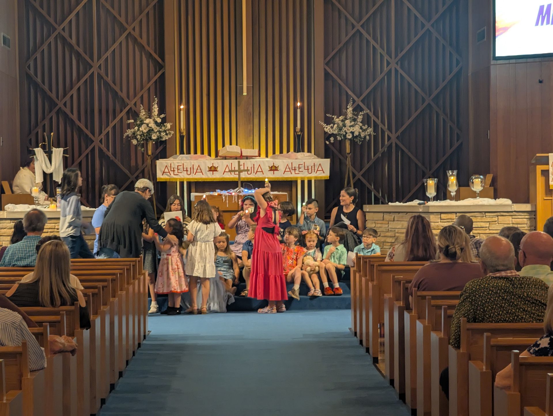Children performing onstage in a church aisle, with pews on both sides and a banner overhead