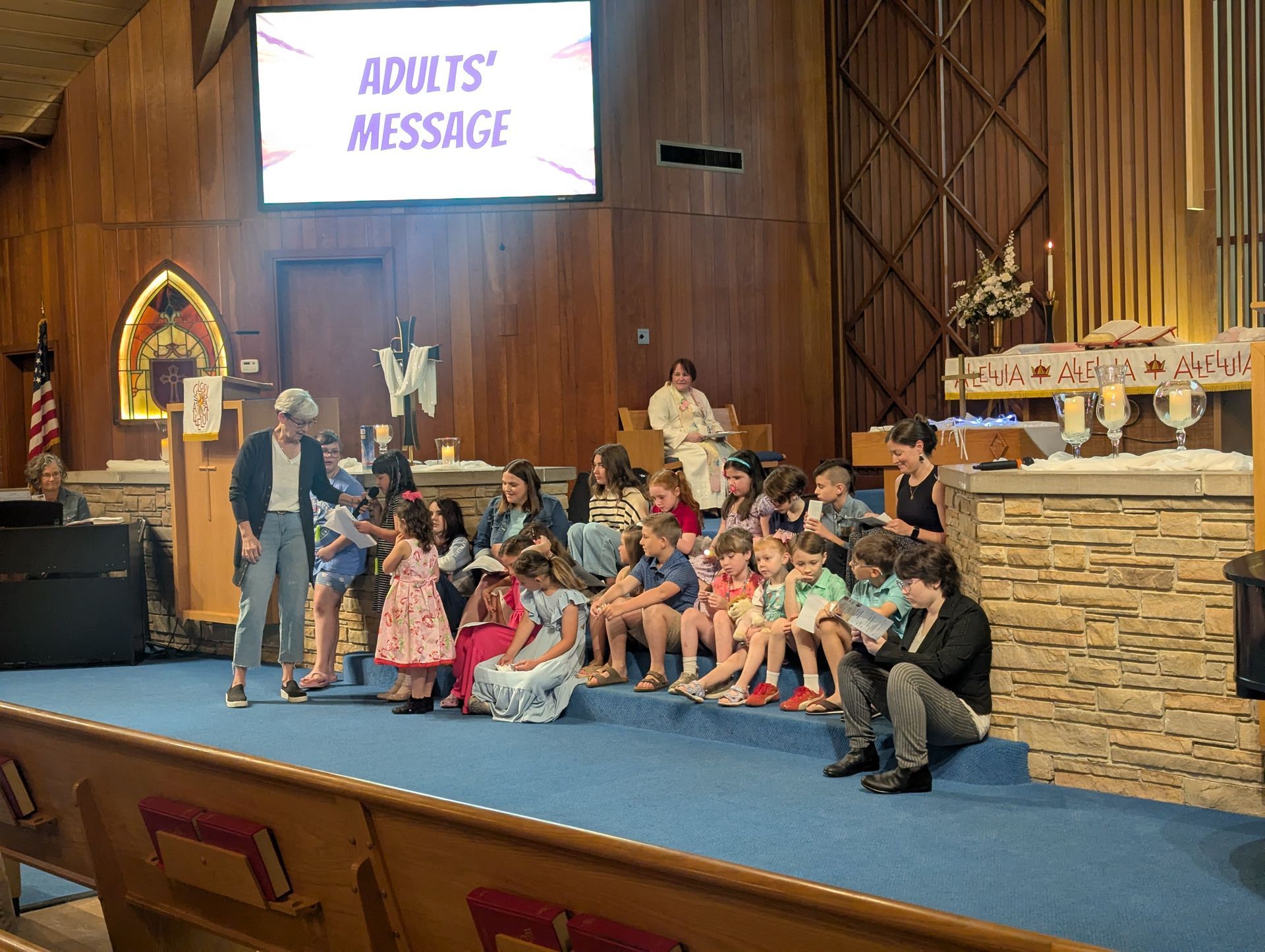 Group seated on a church stage with a “Adults’ Message” sign above them.