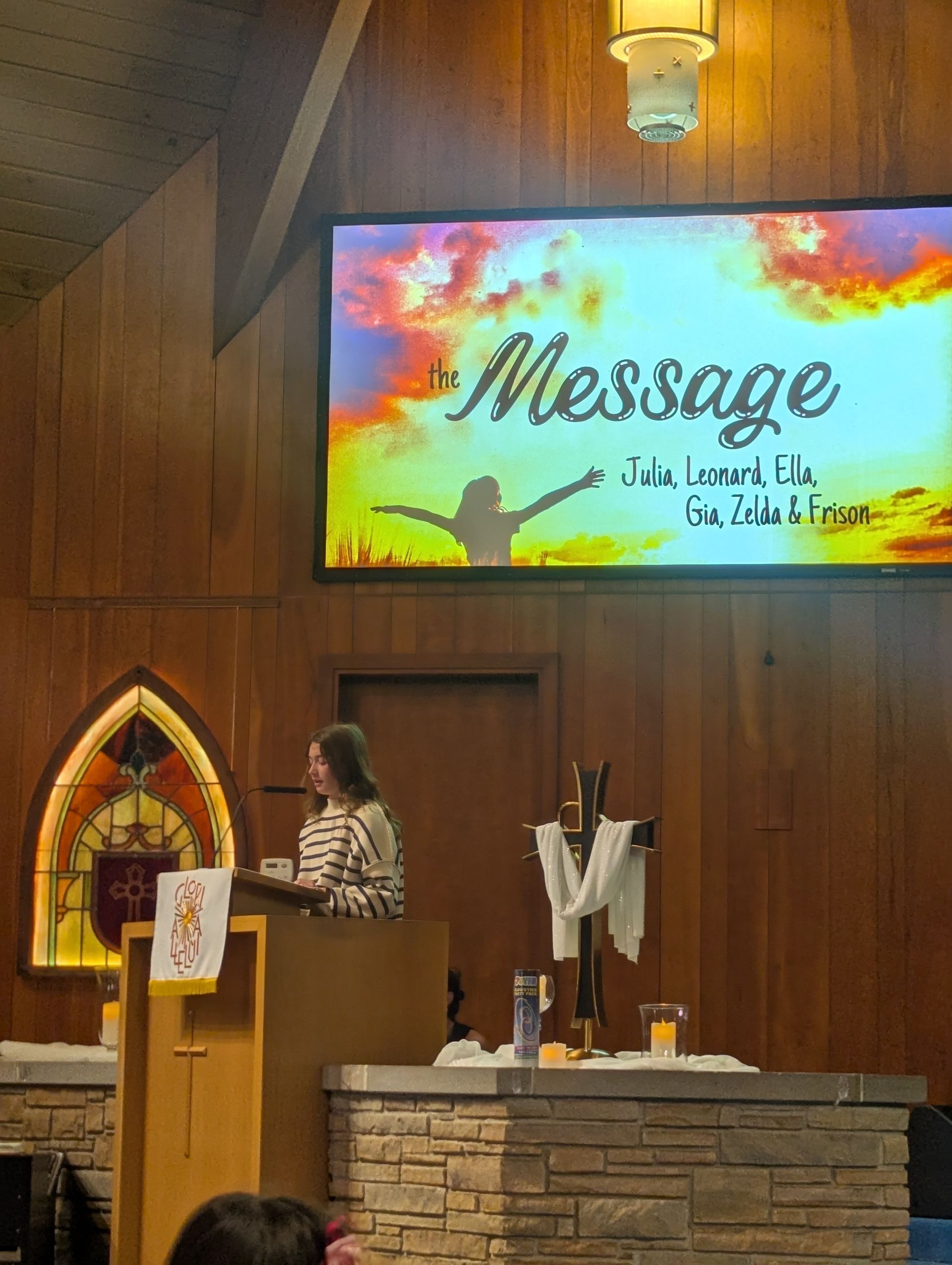 Speaker at church podium beside altar, with colorful “Message” screen in the background