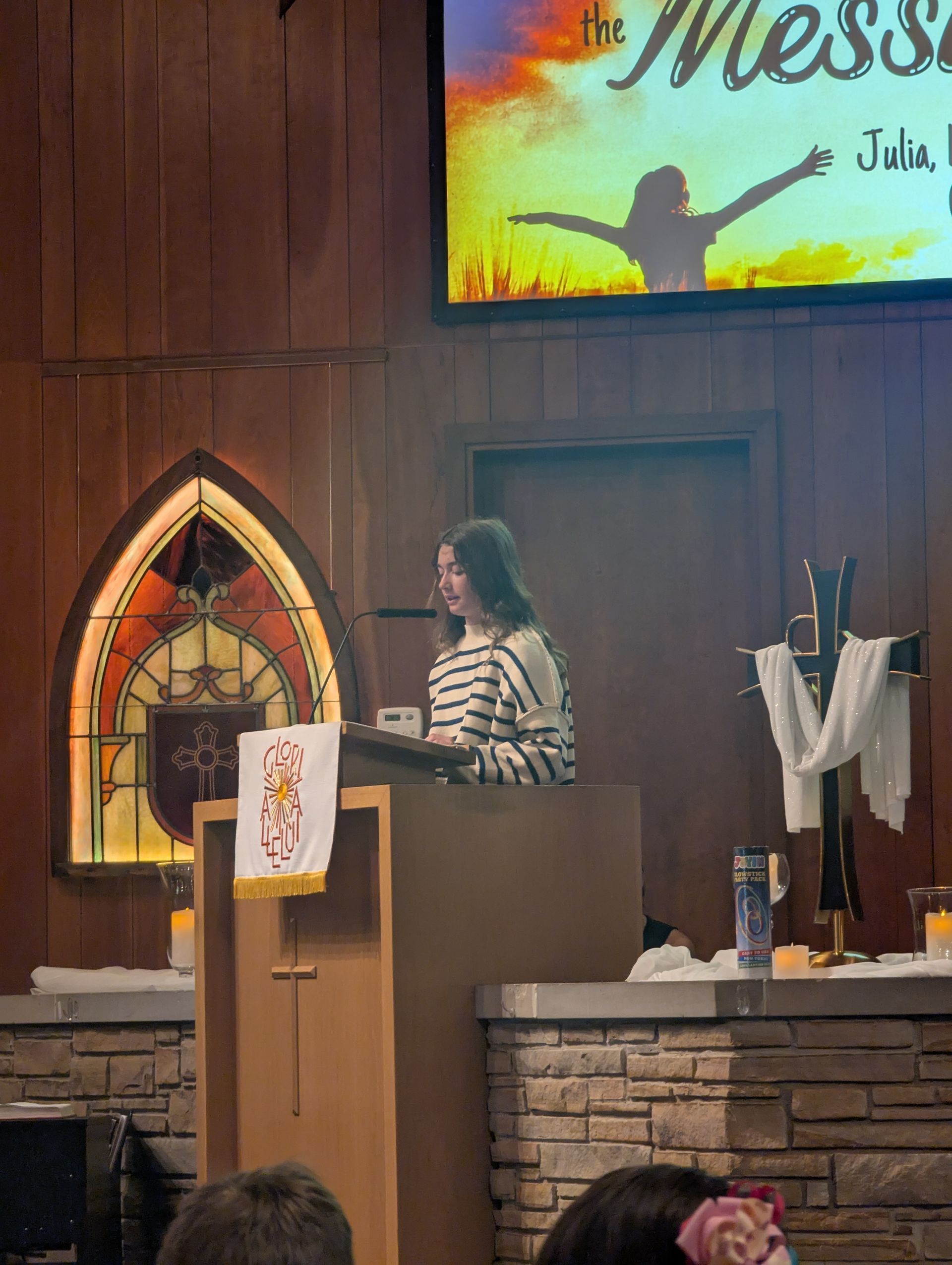 Woman speaking at a church podium beside a stained-glass window and altar during a service