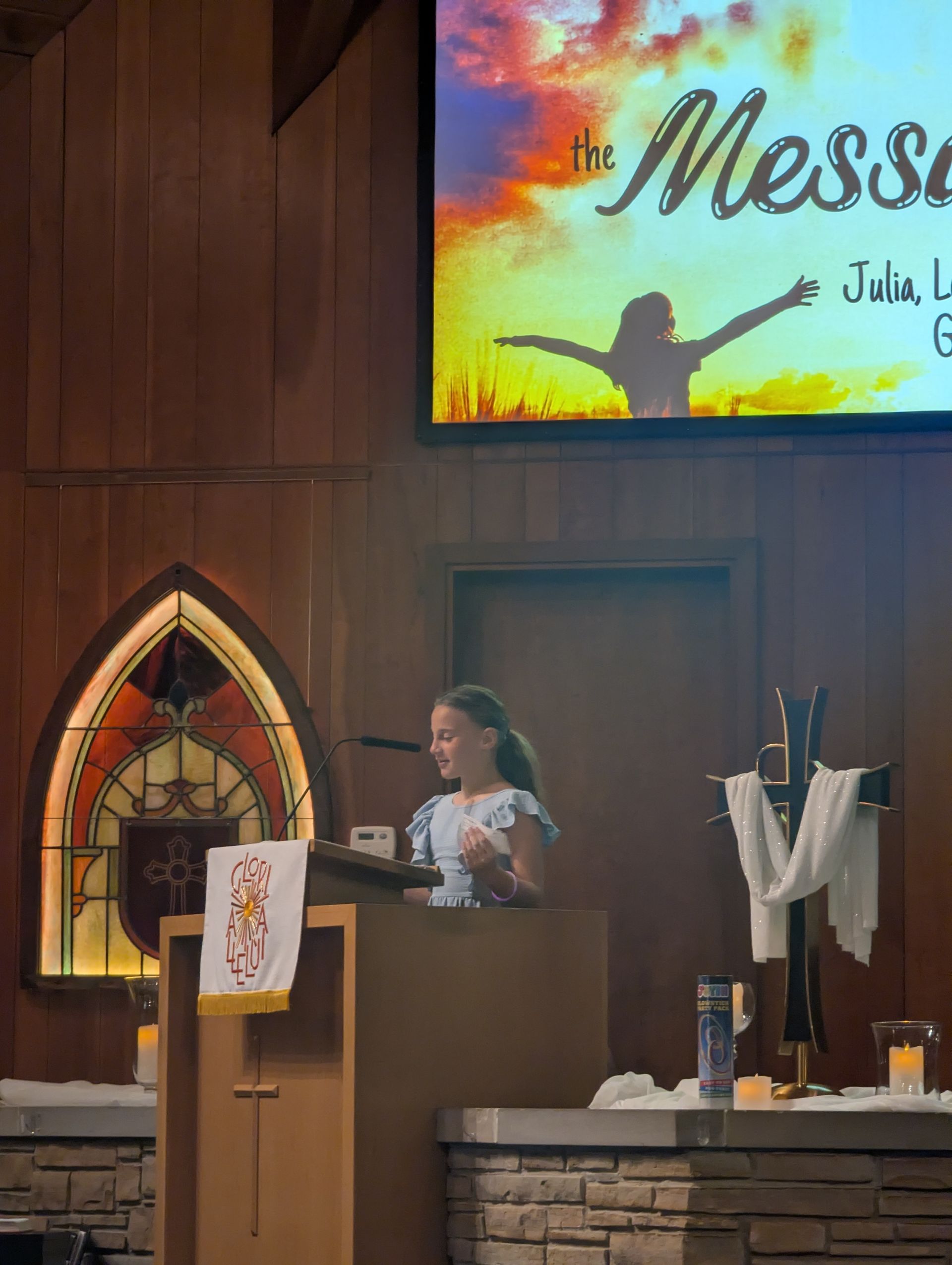 Woman speaking at a church podium beneath a colorful “the Message” screen