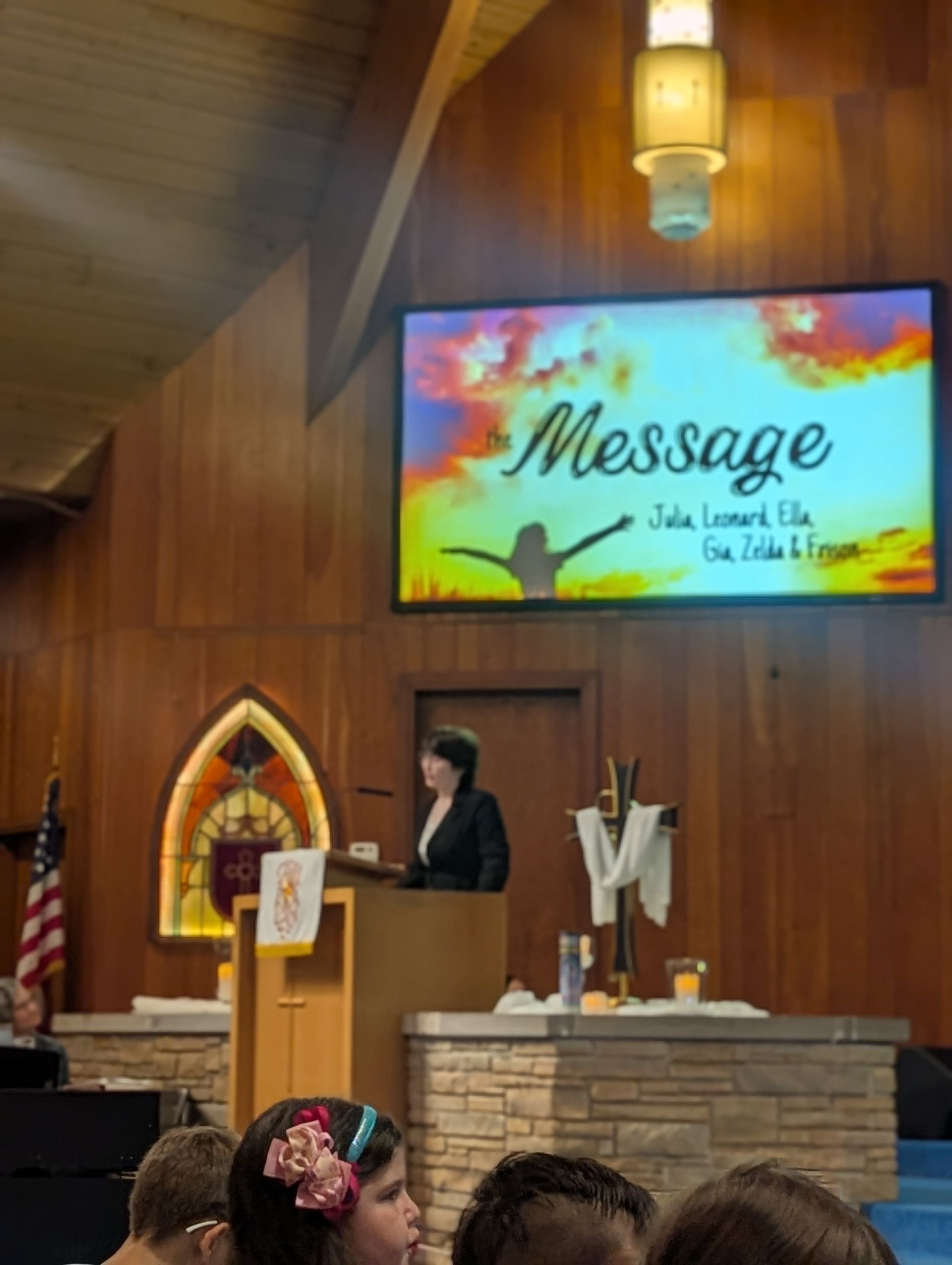 Speaker at church podium beneath colorful “Message” screen in wood-paneled sanctuary