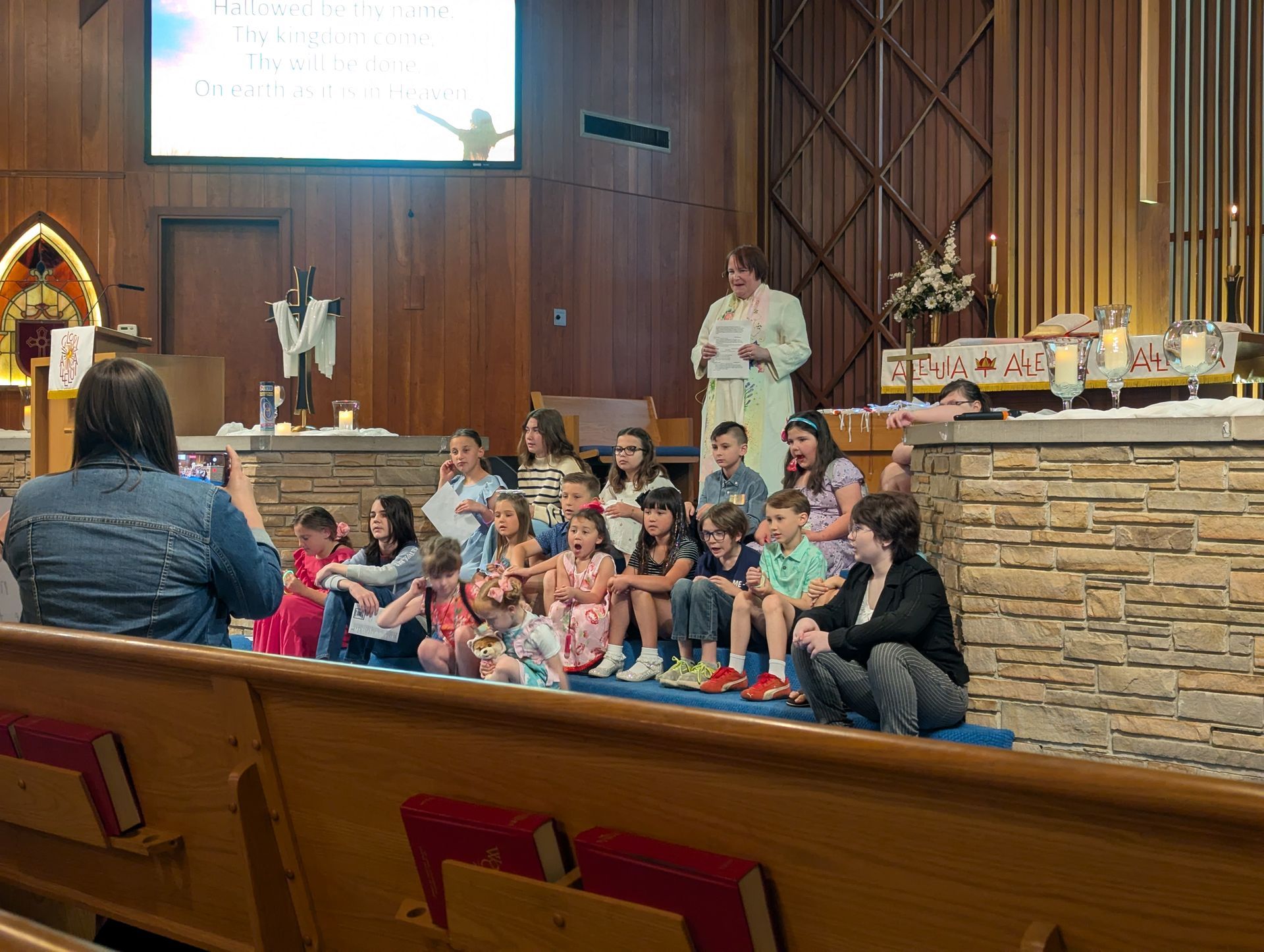 Children seated on steps in a church sanctuary during a group gathering, with adults nearby
