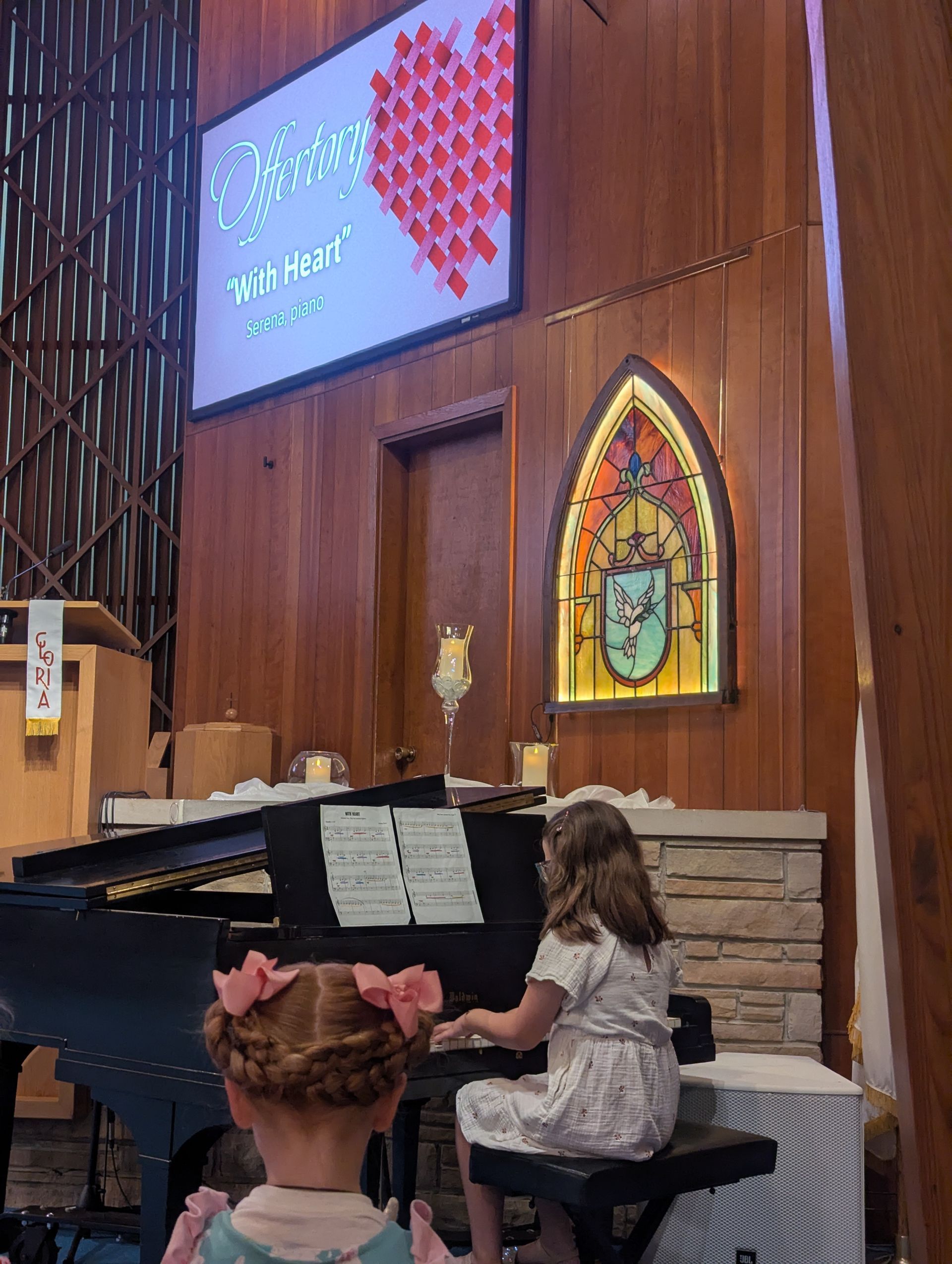 Girl at a piano in a church sanctuary, with a projected screen and stained-glass window behind her.