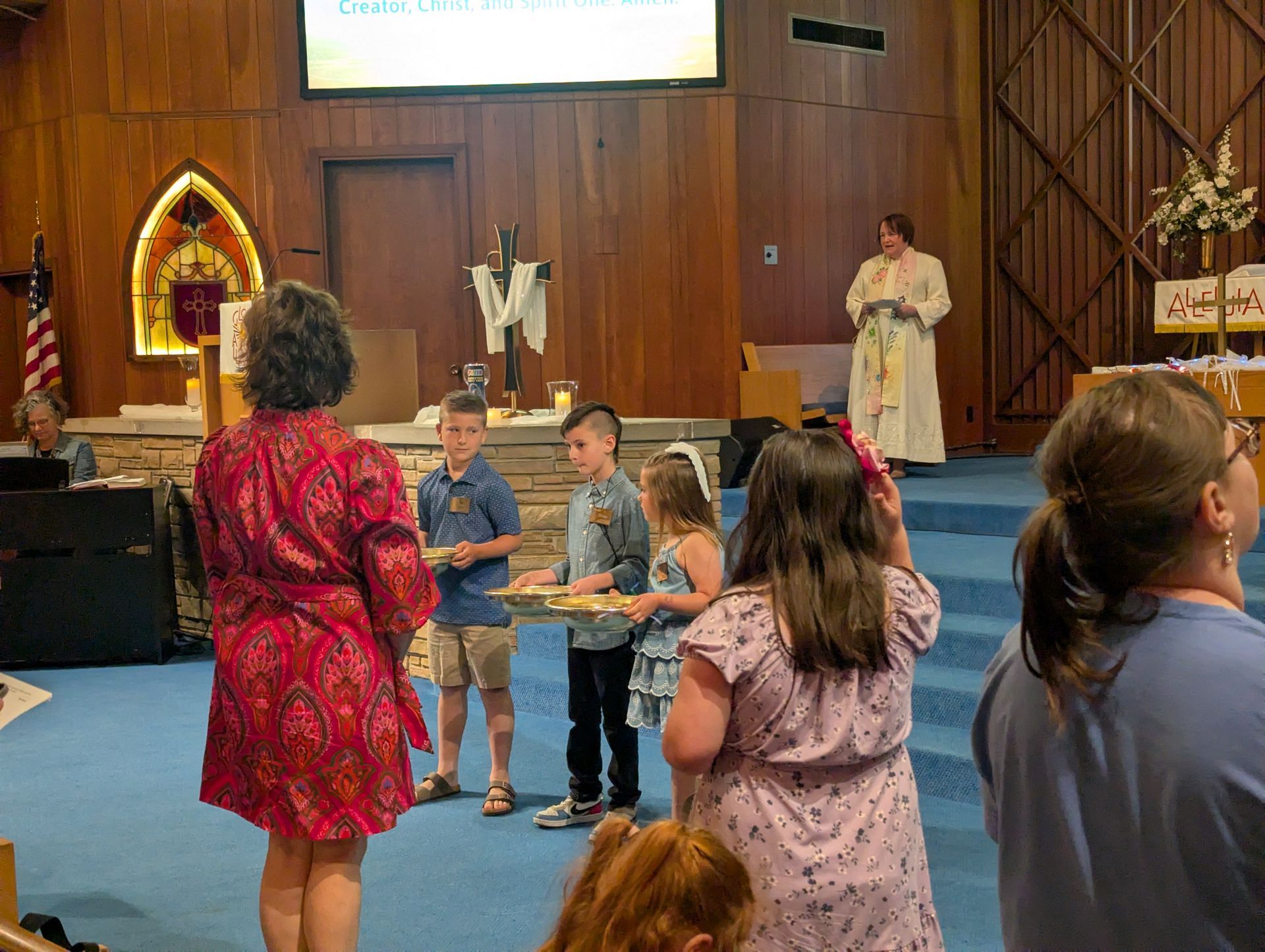 Children standing in a church sanctuary during a gathering, with a speaker at the front.
