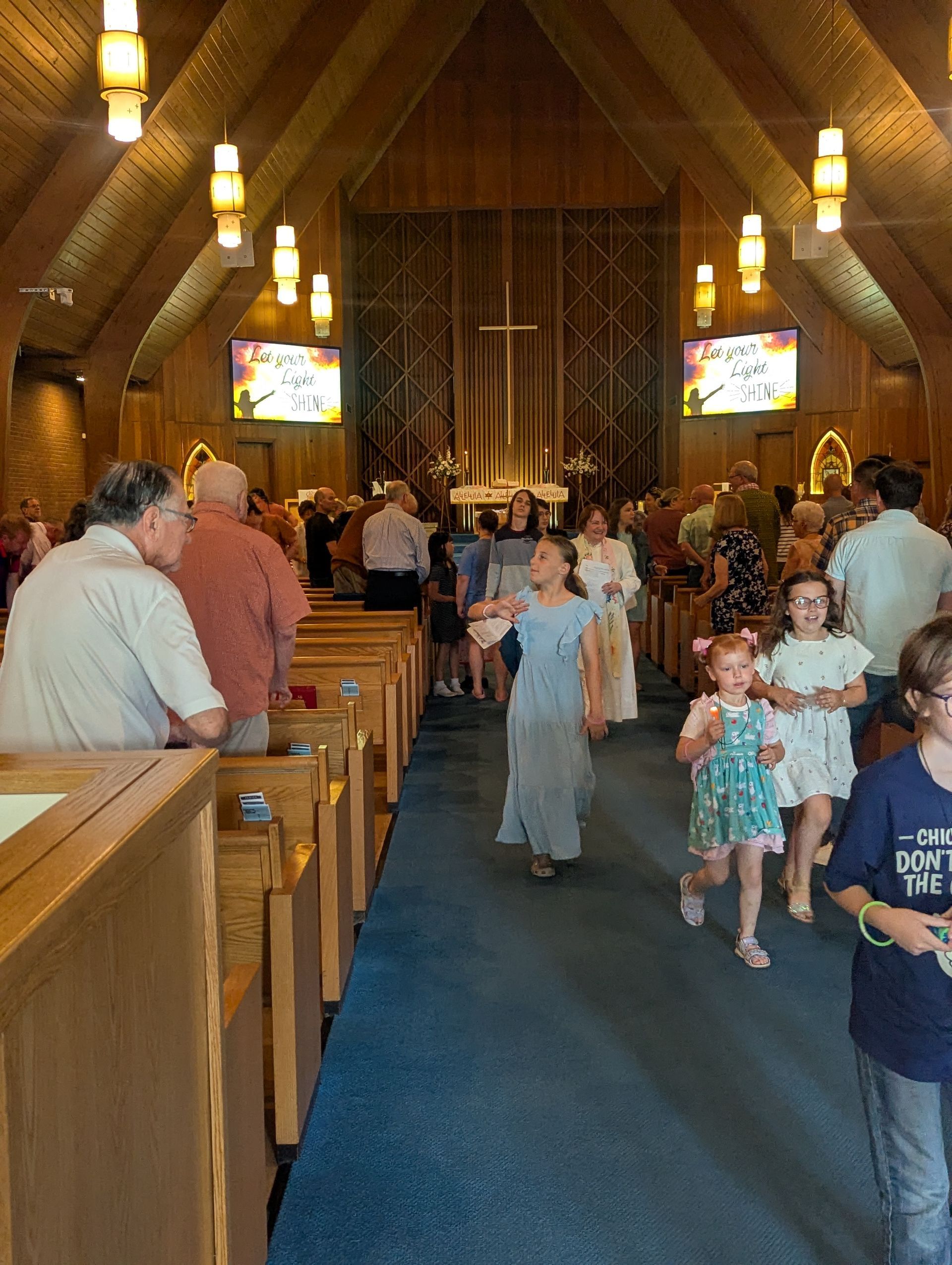Children and adults walking down a blue-carpeted church aisle toward the altar during a service