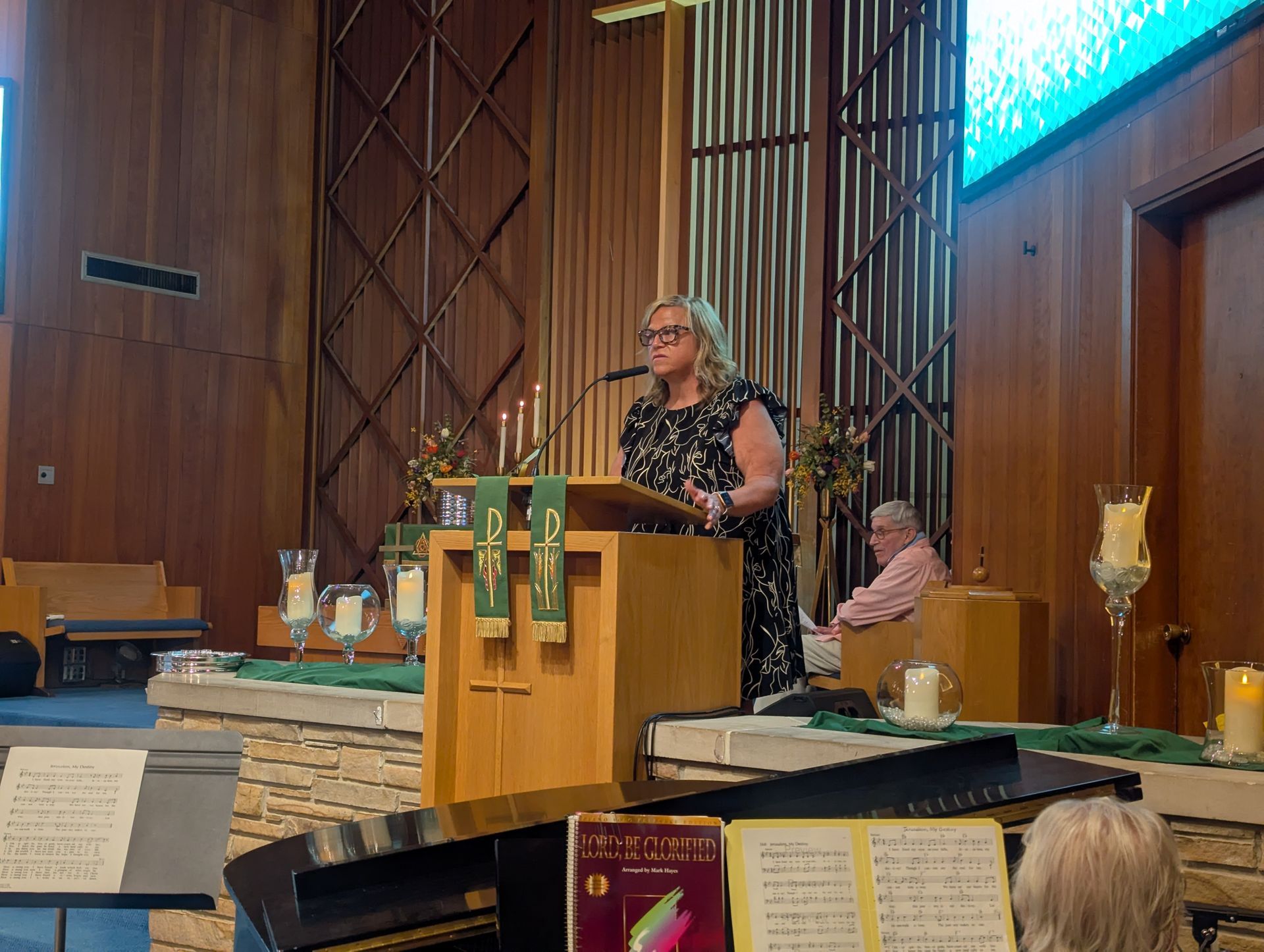 Woman speaking at a church lectern beside altar candles and flowers during a service