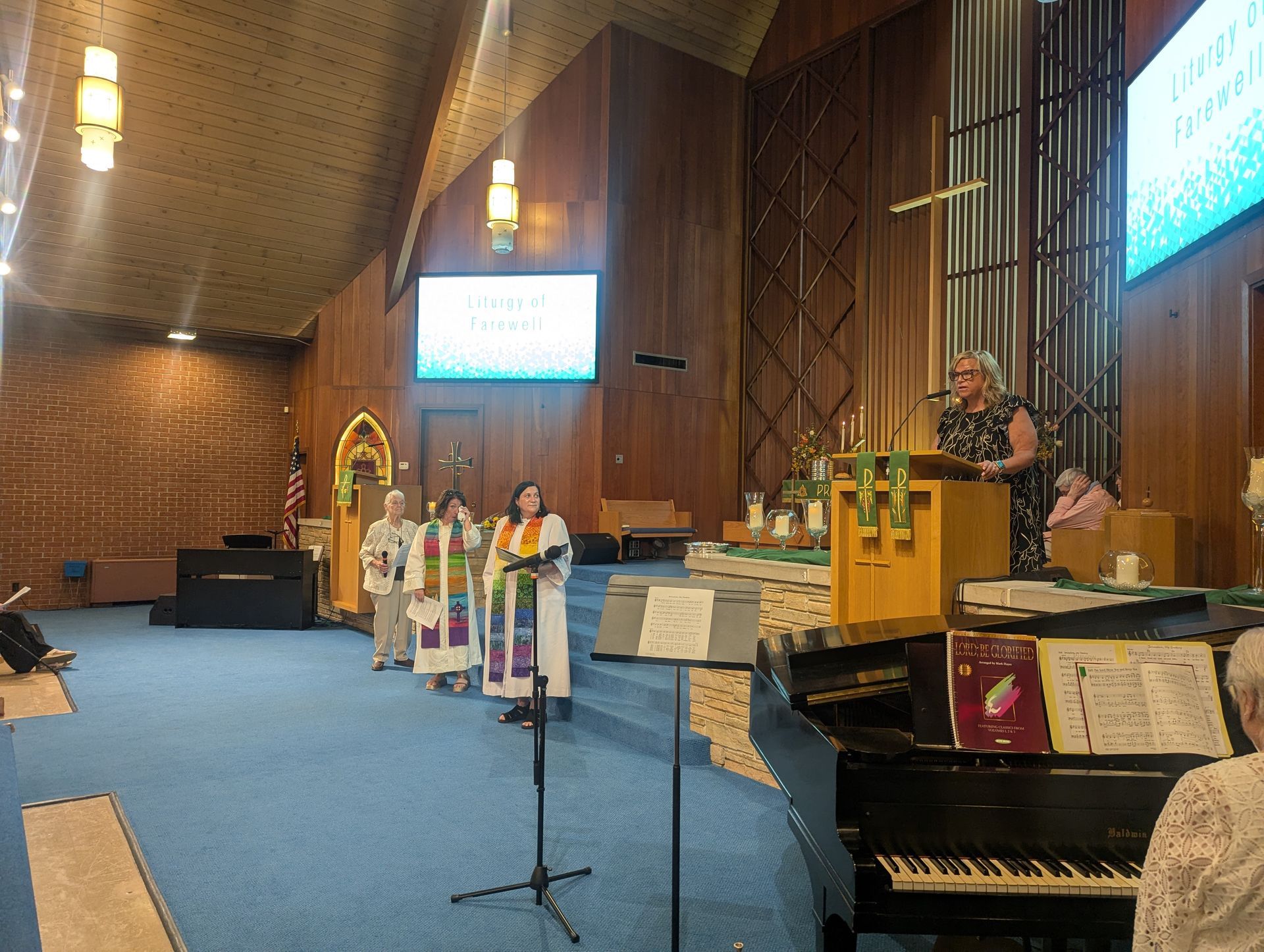 Church sanctuary with clergy at altar, choir mic, piano, and large screen during a service