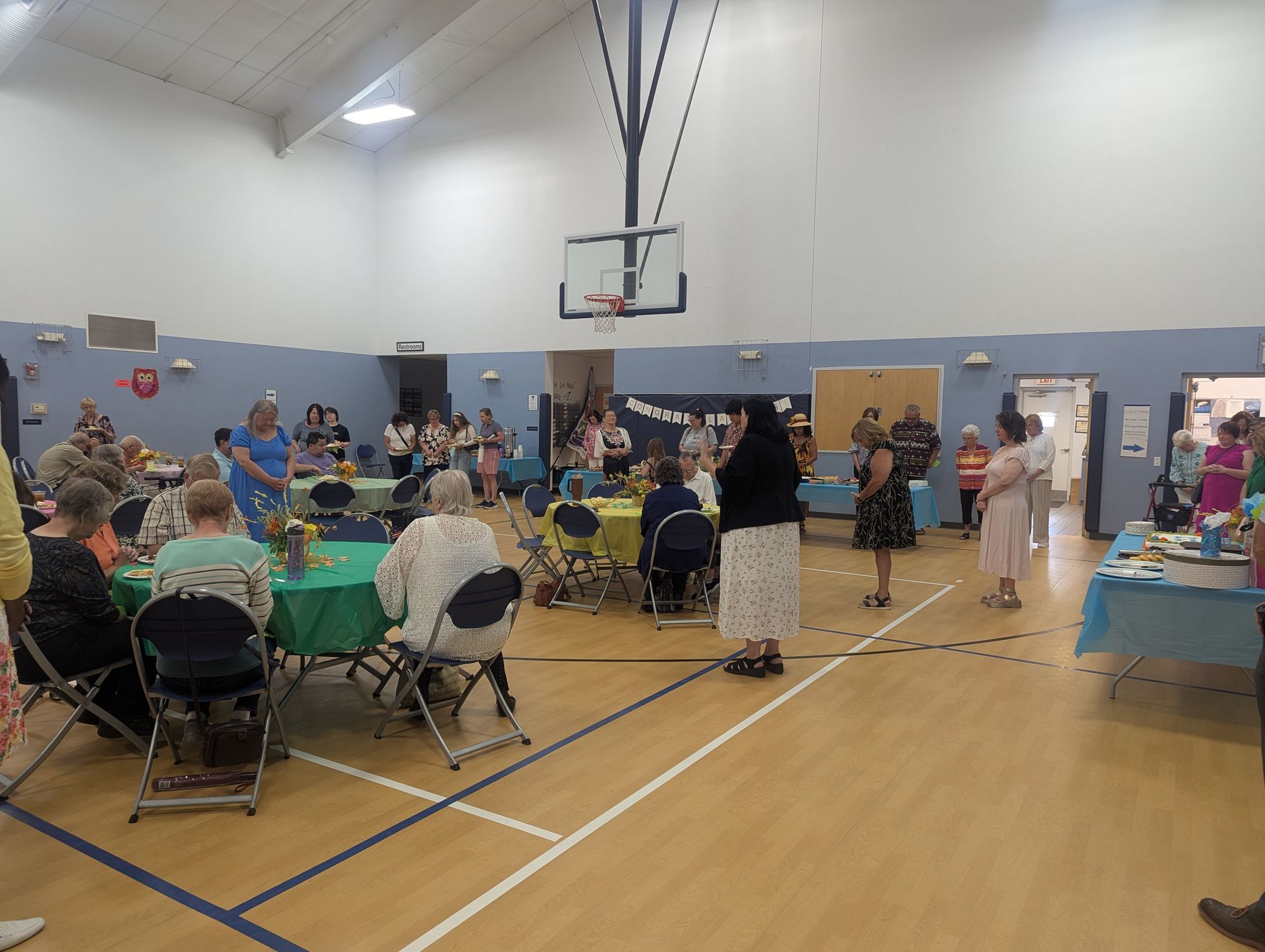 Community event in a gymnasium with tables, seated attendees, and vendors along the walls