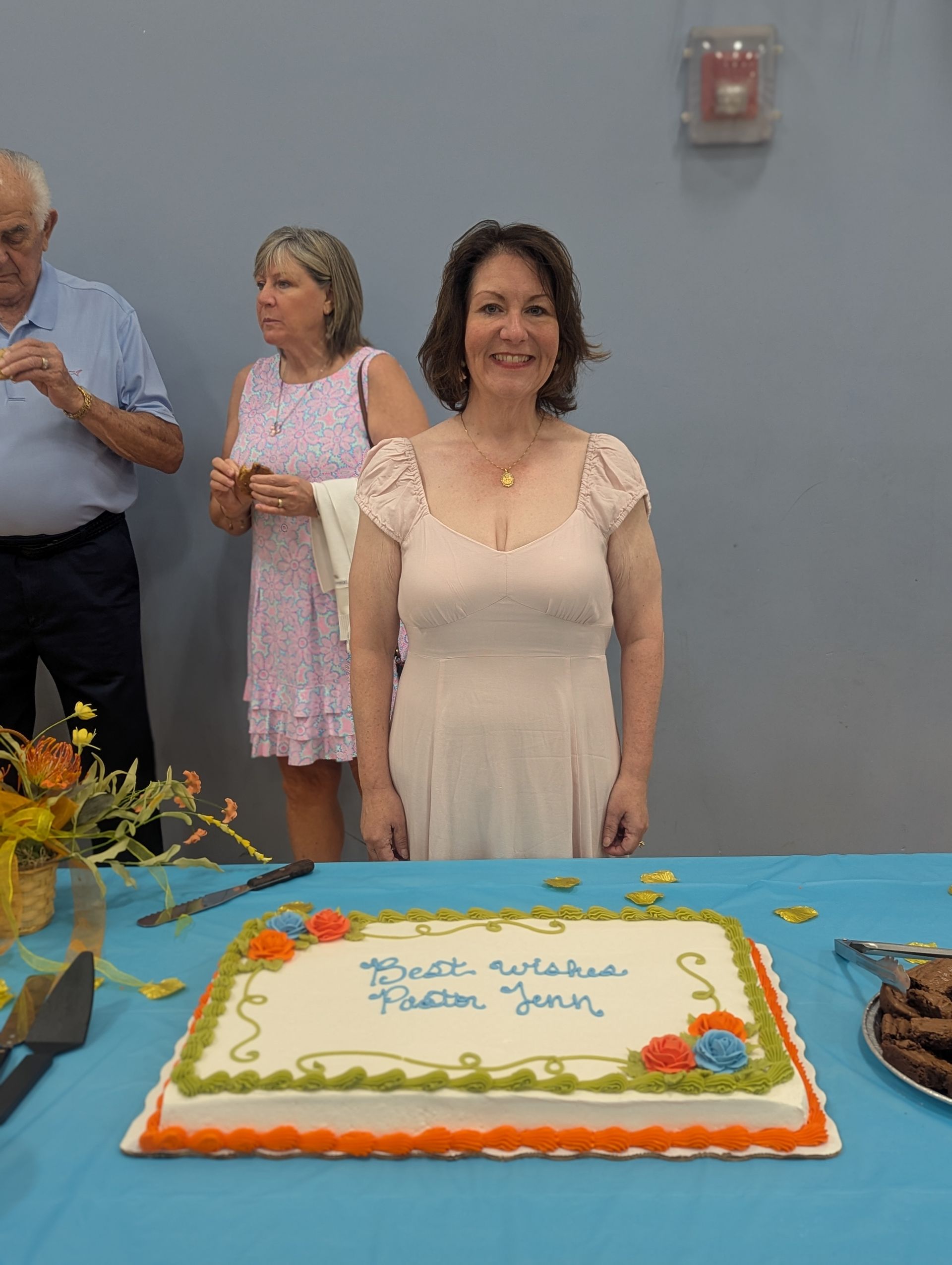 Woman standing behind decorated birthday cake in a room with guests in the background