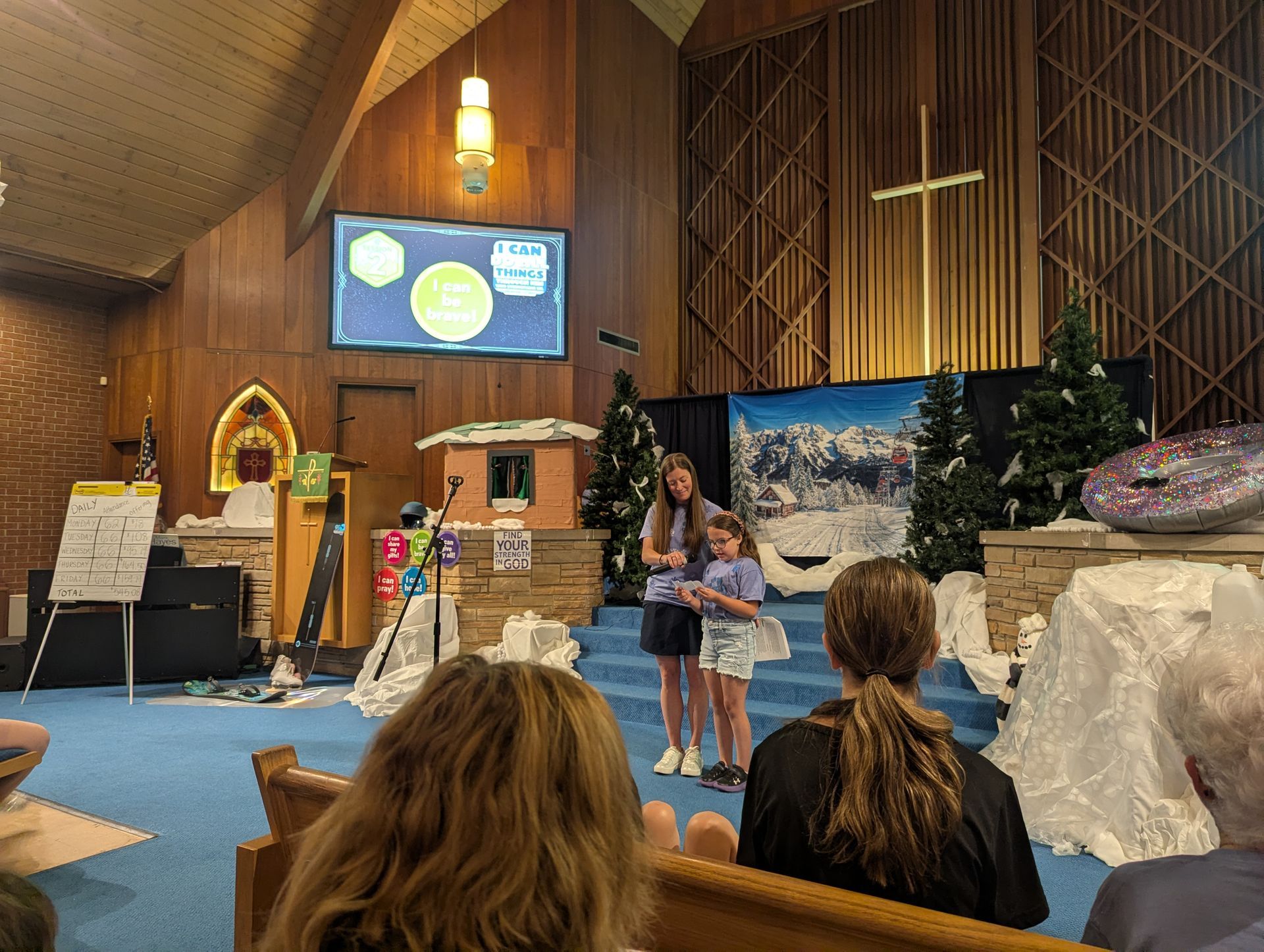 Children speaking on a church stage with a slide projected behind them and audience seated in front.