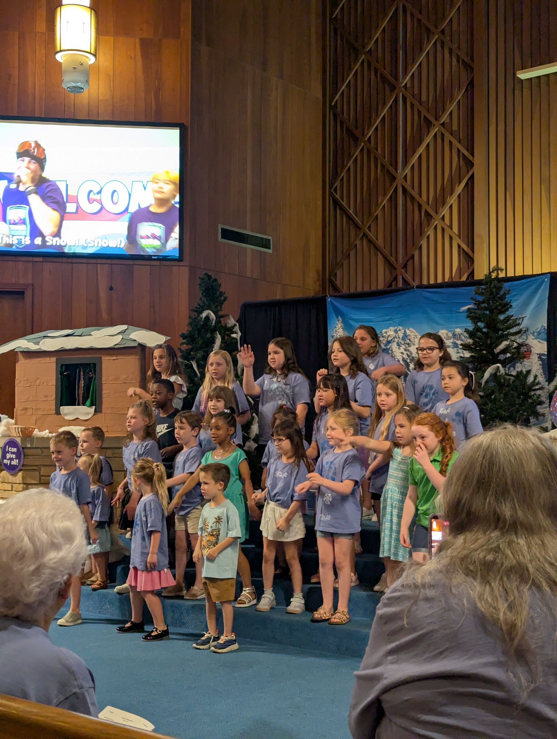 Choir of children and adults on a church stage, singing in front of a blue backdrop