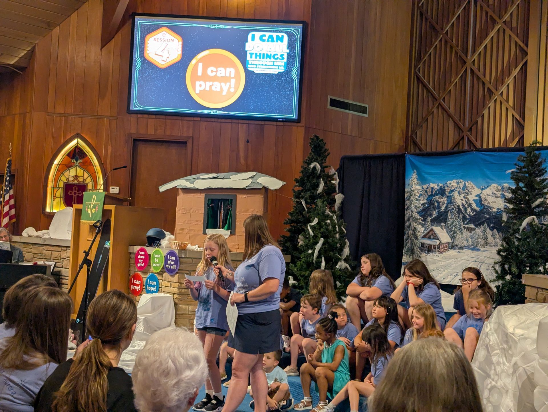 Kids seated onstage at a church event with a “I Can Read!” screen and winter backdrop