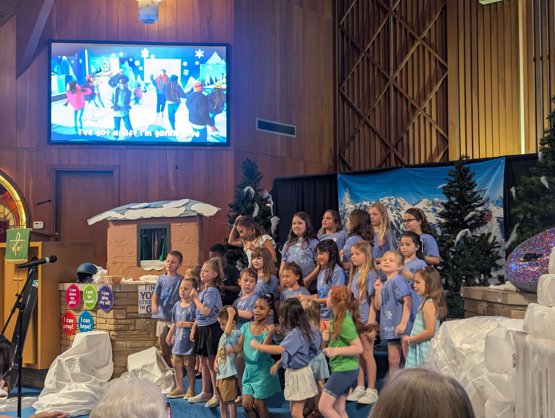 Children posing on a stage with a nativity scene backdrop and a large screen above them