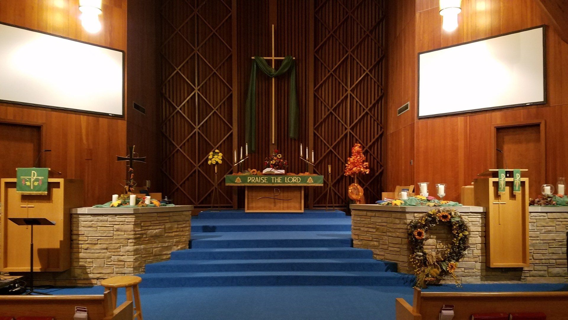 Church altar with blue carpeted steps, wooden walls, candles, and green liturgical decorations