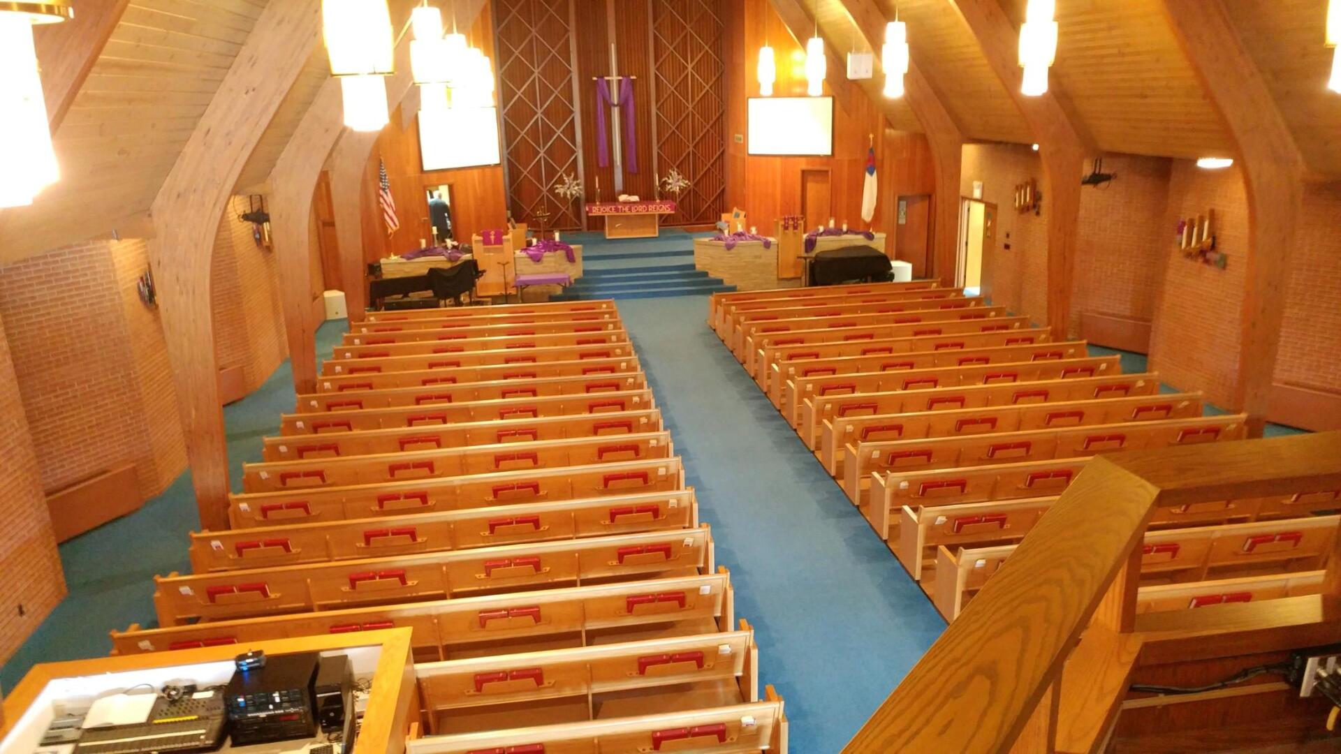 Interior of a wooden church with rows of pews and a blue aisle leading to the altar.