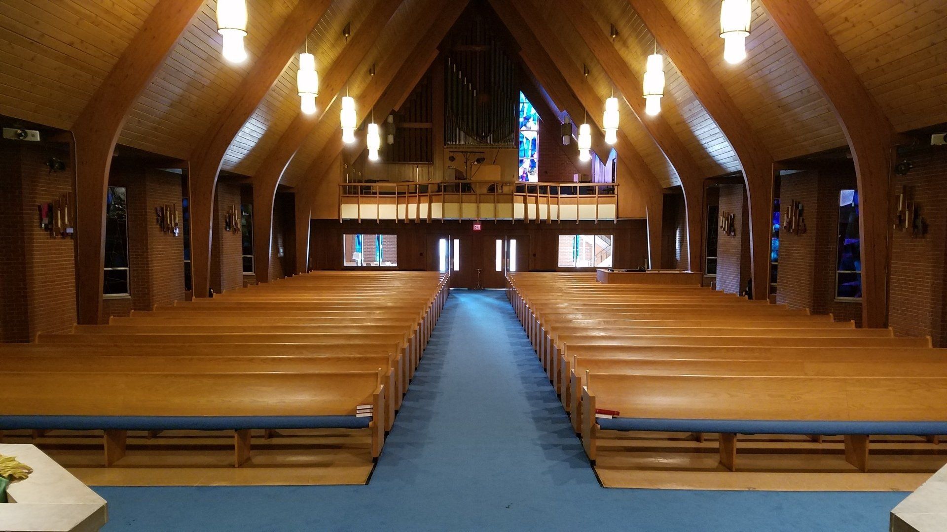 Wooden church interior with rows of pews, blue carpeted aisle, and stained glass windows at the far end