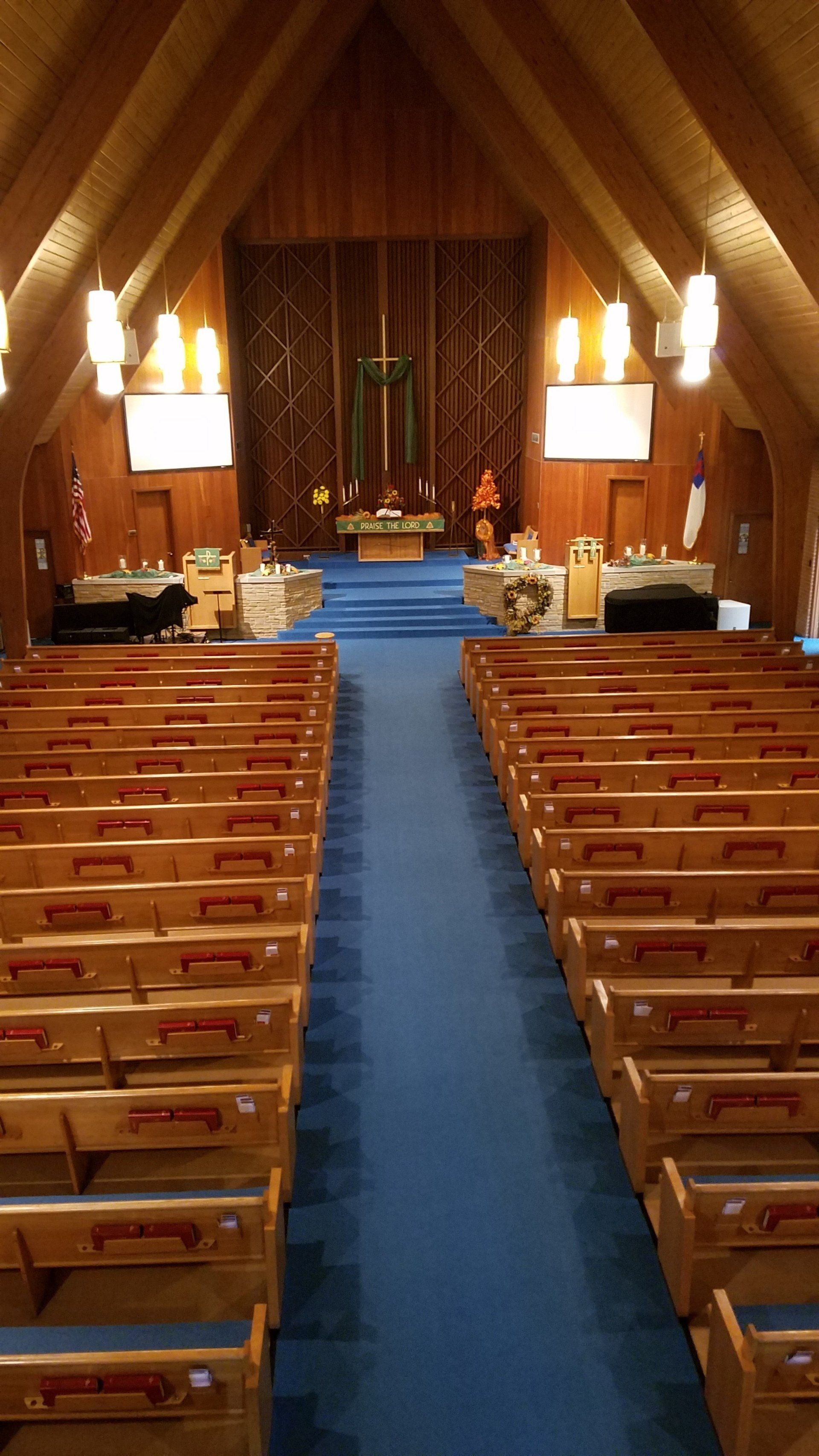 Empty church interior with wooden pews, blue carpet aisle, and altar at the front