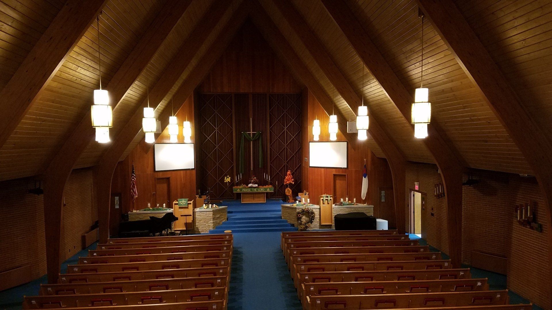 Interior of a wooden church sanctuary with pews, hanging lights, and a blue aisle leading to the altar