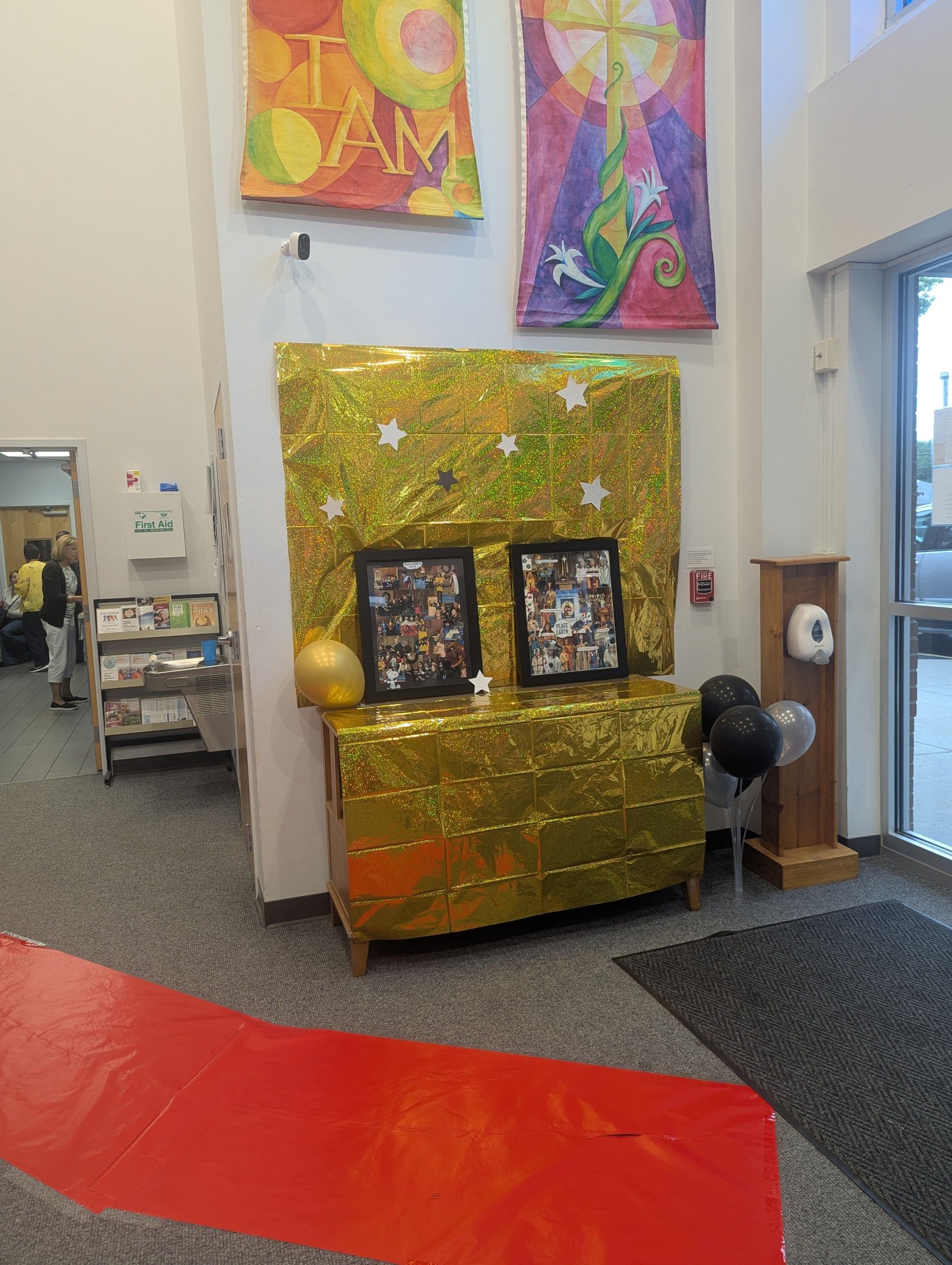 Colorful hallway display with gold backdrop, framed photos, balloons, and a red carpet runner