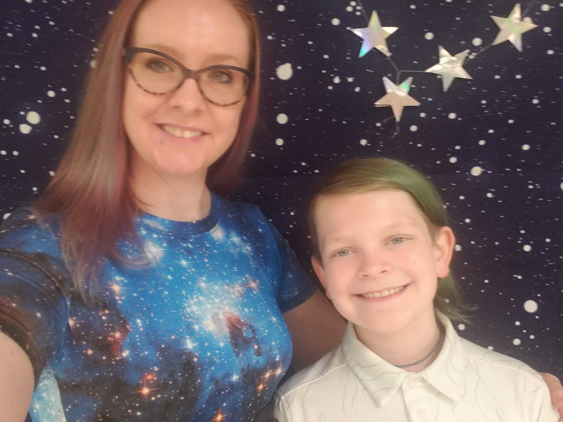 Two people smiling before a starry backdrop, wearing galaxy-print and white shirts