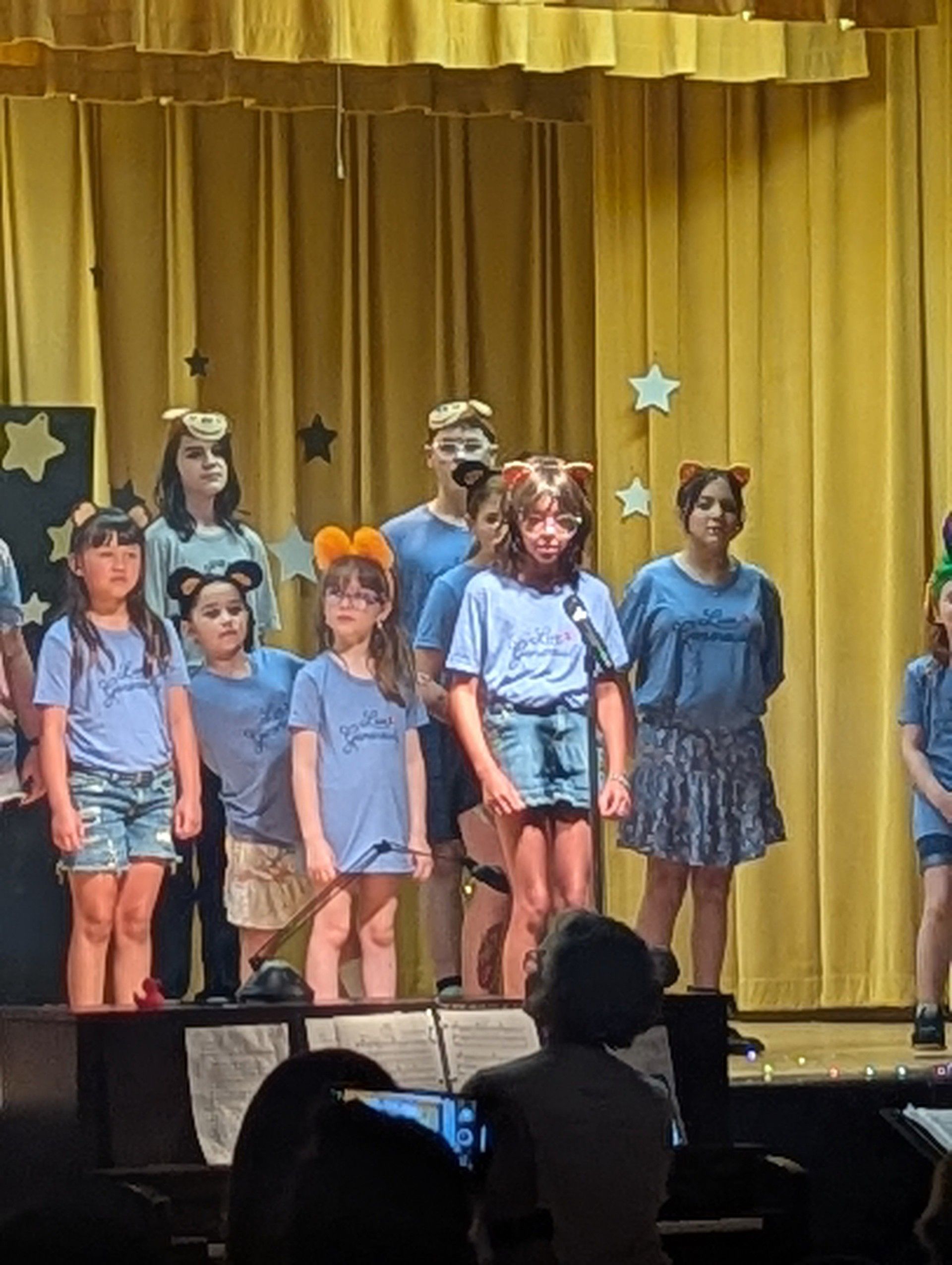 Children on a stage with gold curtains, standing in costume during a performance.