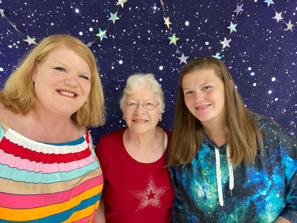 Three smiling people standing before a starry purple backdrop, wearing colorful tops
