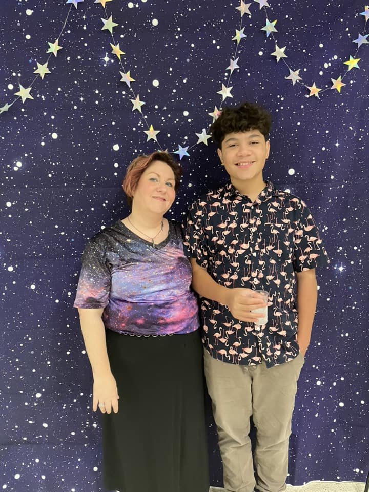 Two people standing together in front of a starry purple backdrop, smiling and posing.