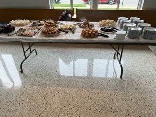 Dessert buffet table with trays of pastries and stacks of silver cups in a bright room.