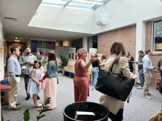 People mingling in a bright indoor courtyard with skylight, plants, and a reception-style gathering