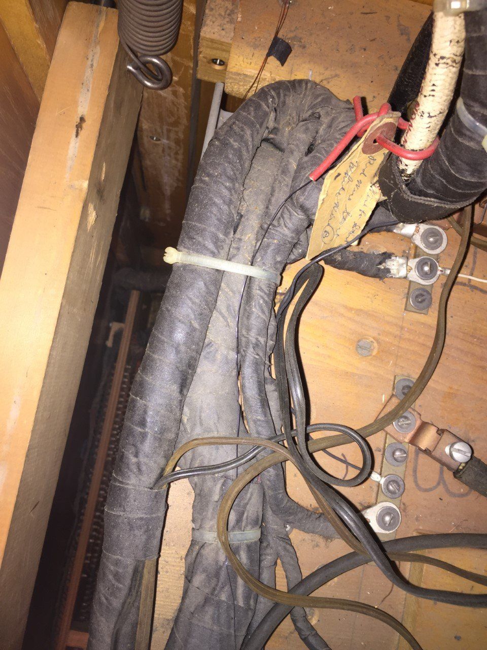 Bundled black cables and wires tied together inside a wooden utility cabinet.