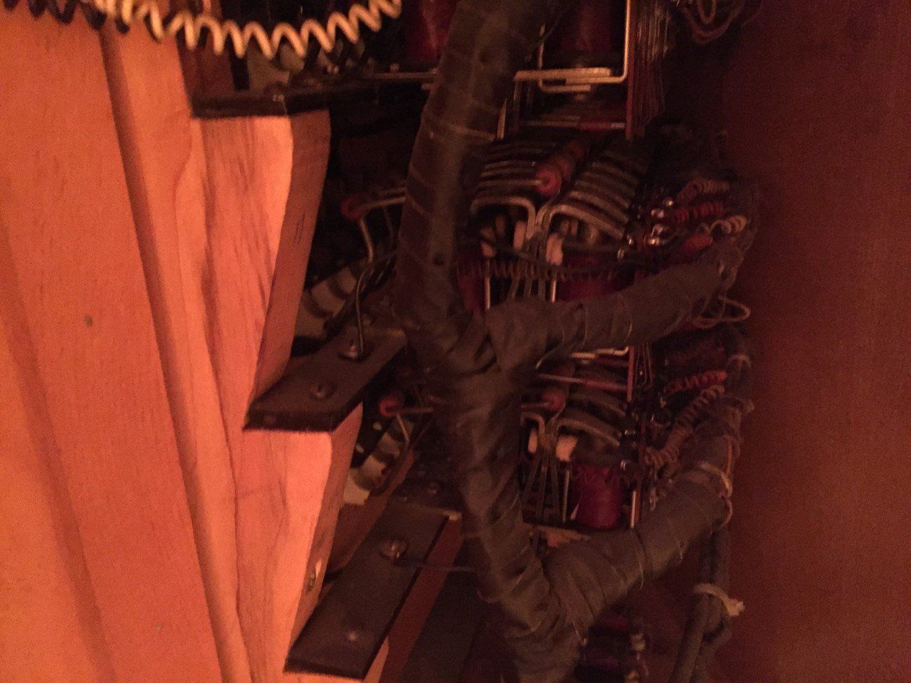 Close-up of a wall-mounted circuit board with wires and components inside a wooden cabinet
