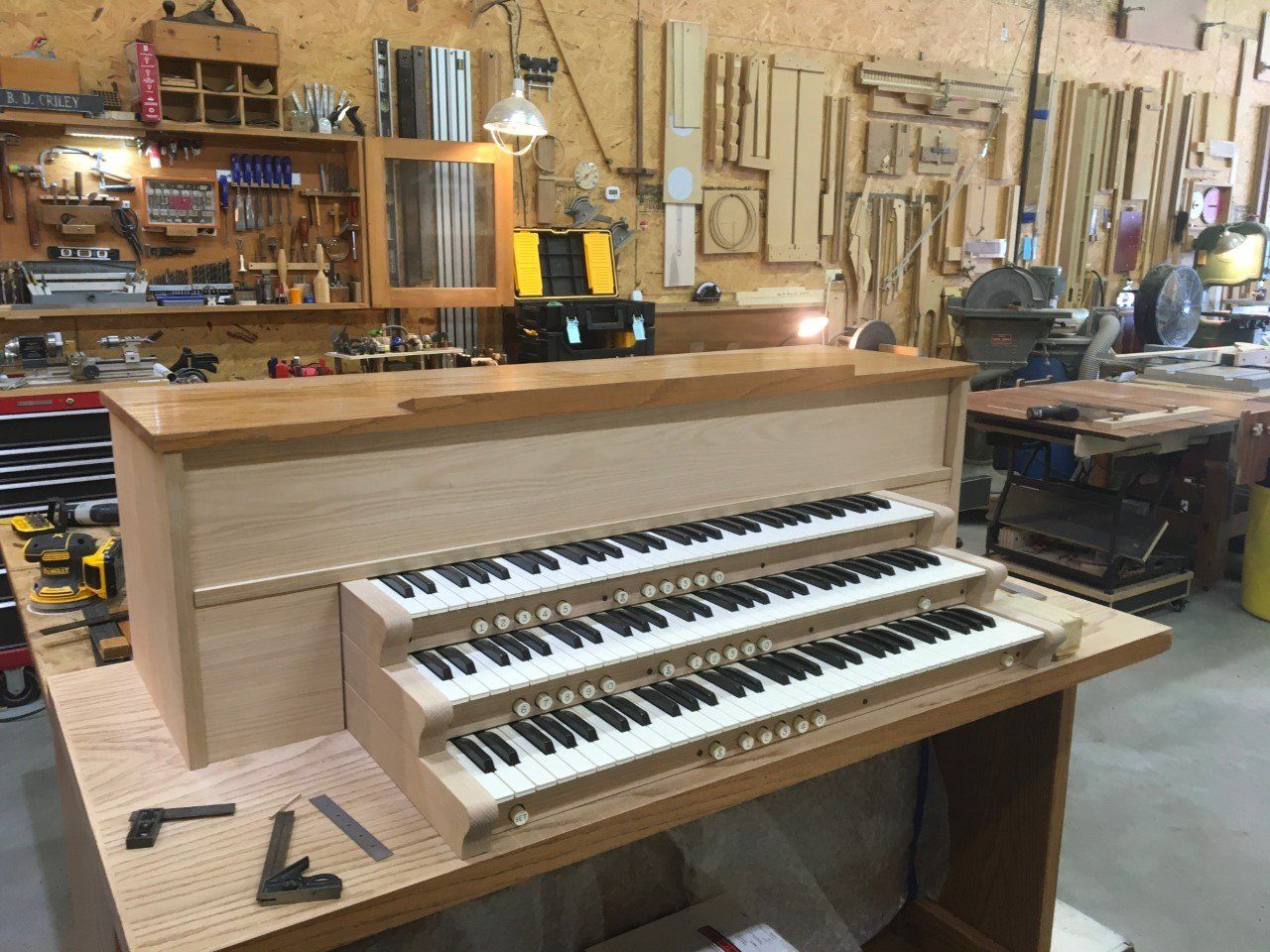 Wooden pipe organ console with two keyboards in a workshop, surrounded by tools and wooden parts.