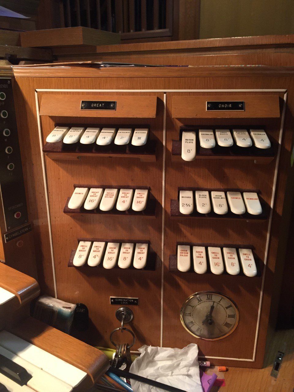 Wooden pipe organ console with rows of white stop tabs and a pedal keyboard below