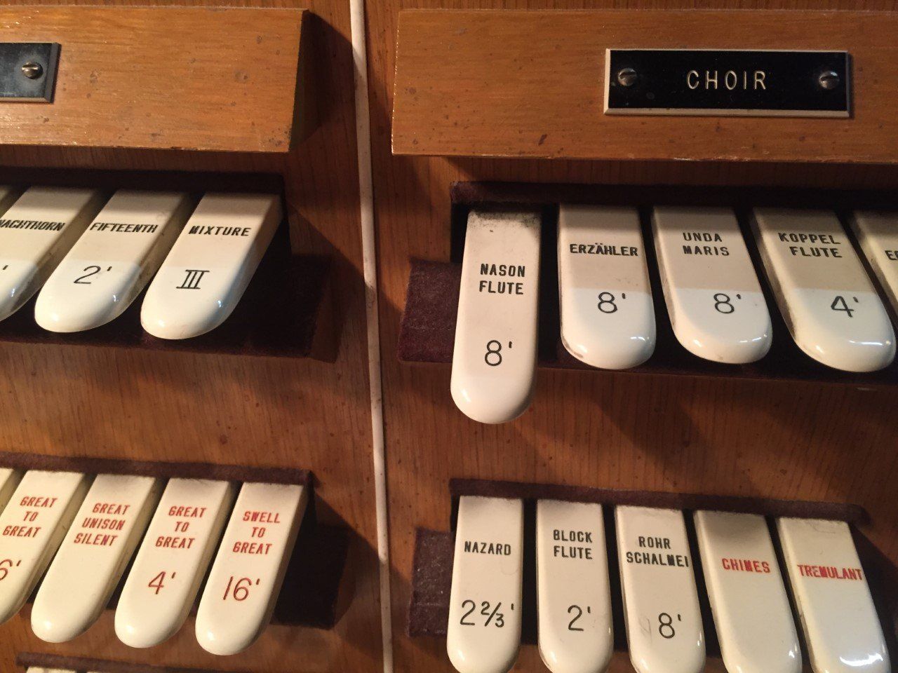 Close-up of organ stops labeled Choir, with white and black tabs on a wooden console.