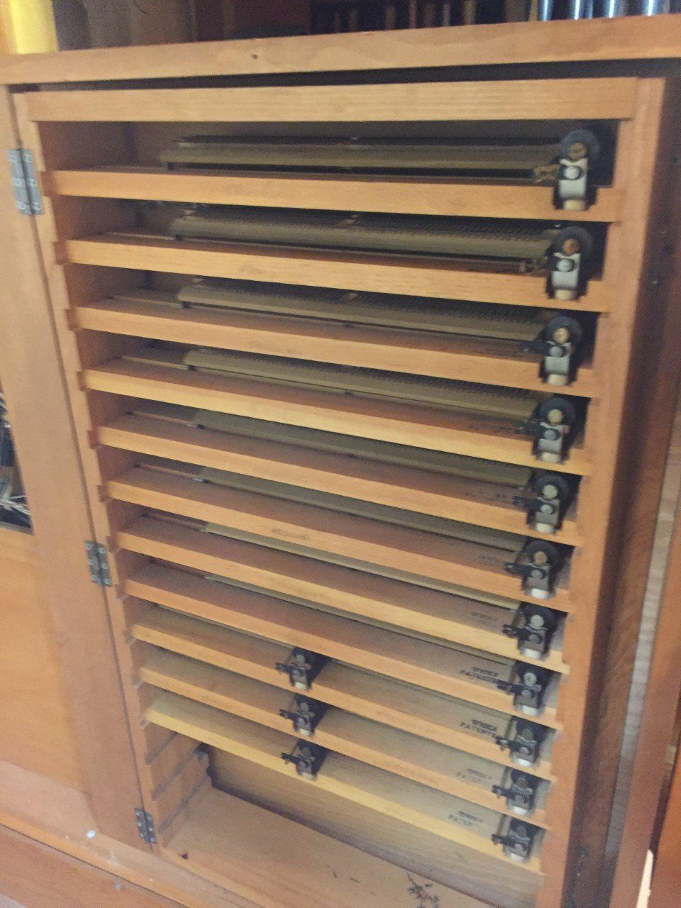 Wooden cabinet with several horizontal metal trays or shelves partially pulled out, viewed from the front.