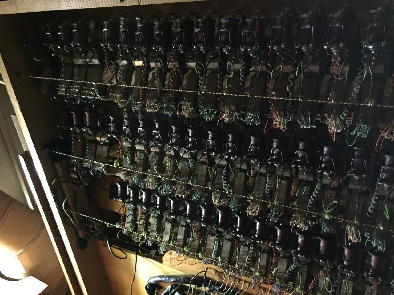 Rows of wired electronic components mounted on a wall, lit by a lamp in a dim room