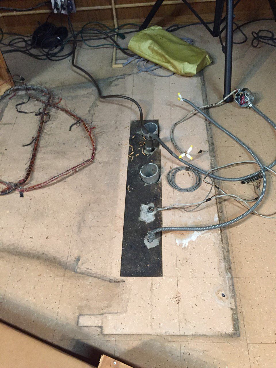 Floor with tangled cables, a power strip, and a green bag under a table.