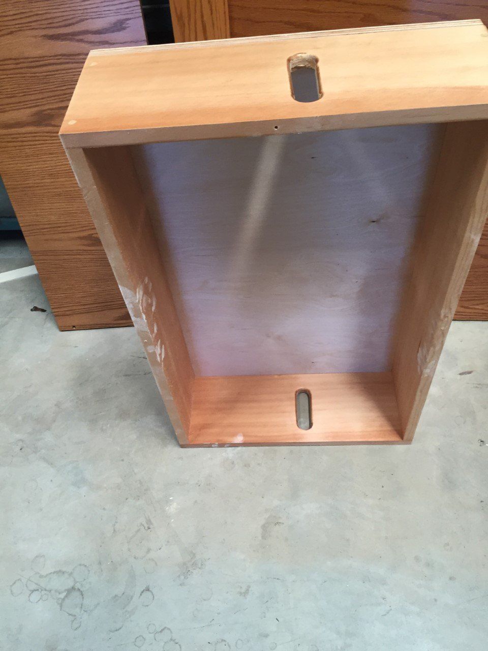 Open wooden box or cabinet lying on its side on a concrete floor.