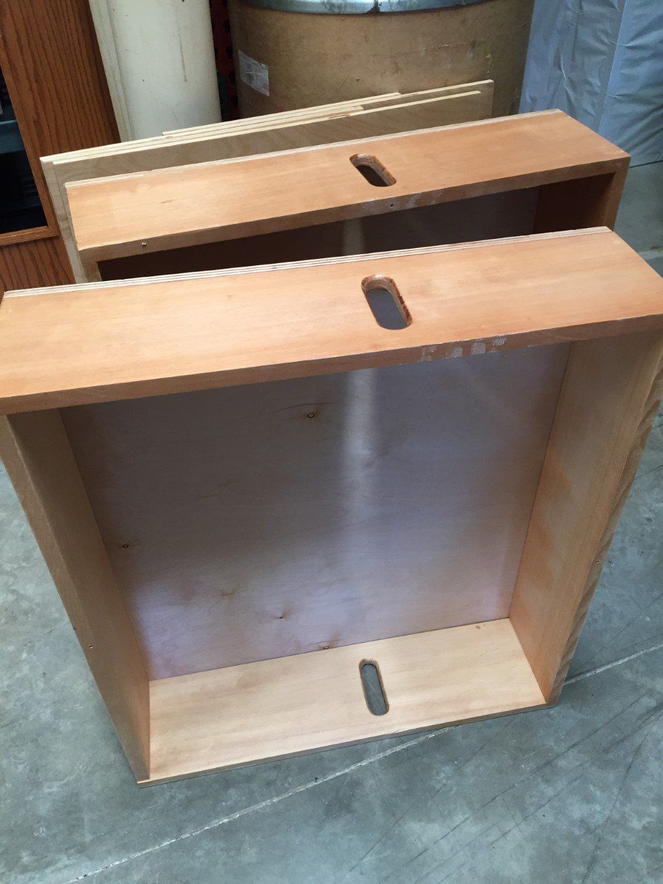 Two wooden boxes with metal panels, stacked in a workshop on a concrete floor.