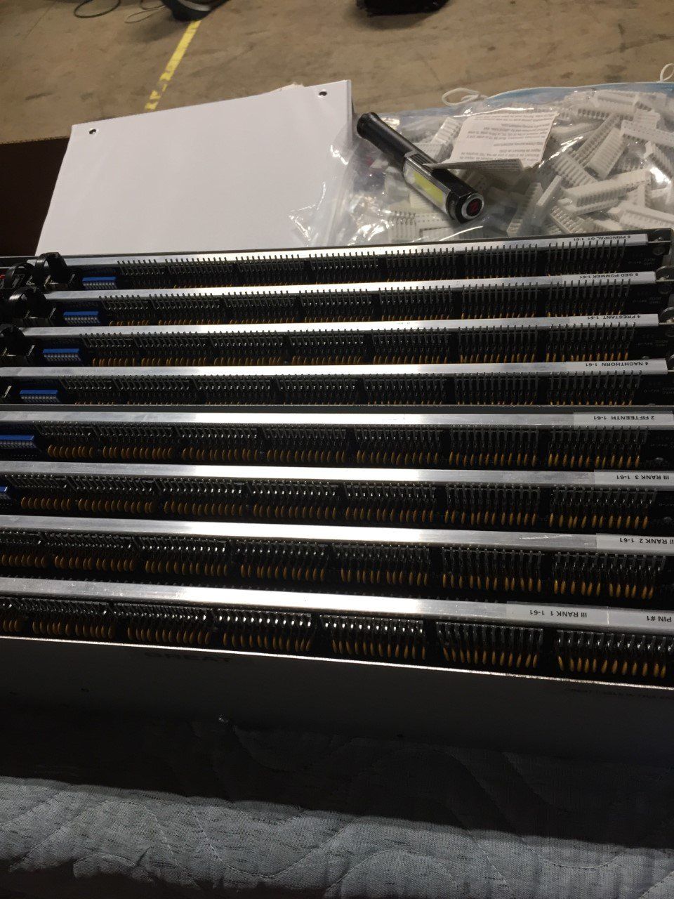 Stack of black keyboard strip components with white markings on a workbench, next to bags of small parts.